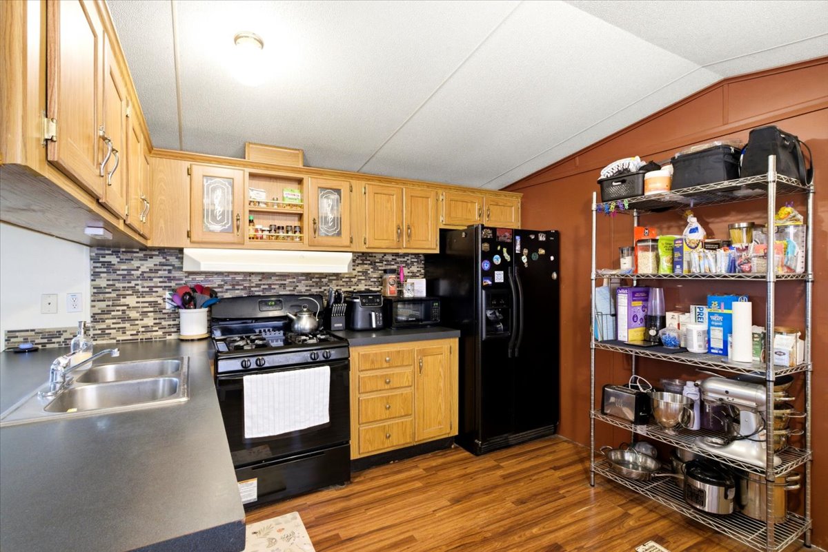 Kitchen featuring wood-finish flooring, a double basin stainless steel sink, black gas range, and a mosaic tile backsplash