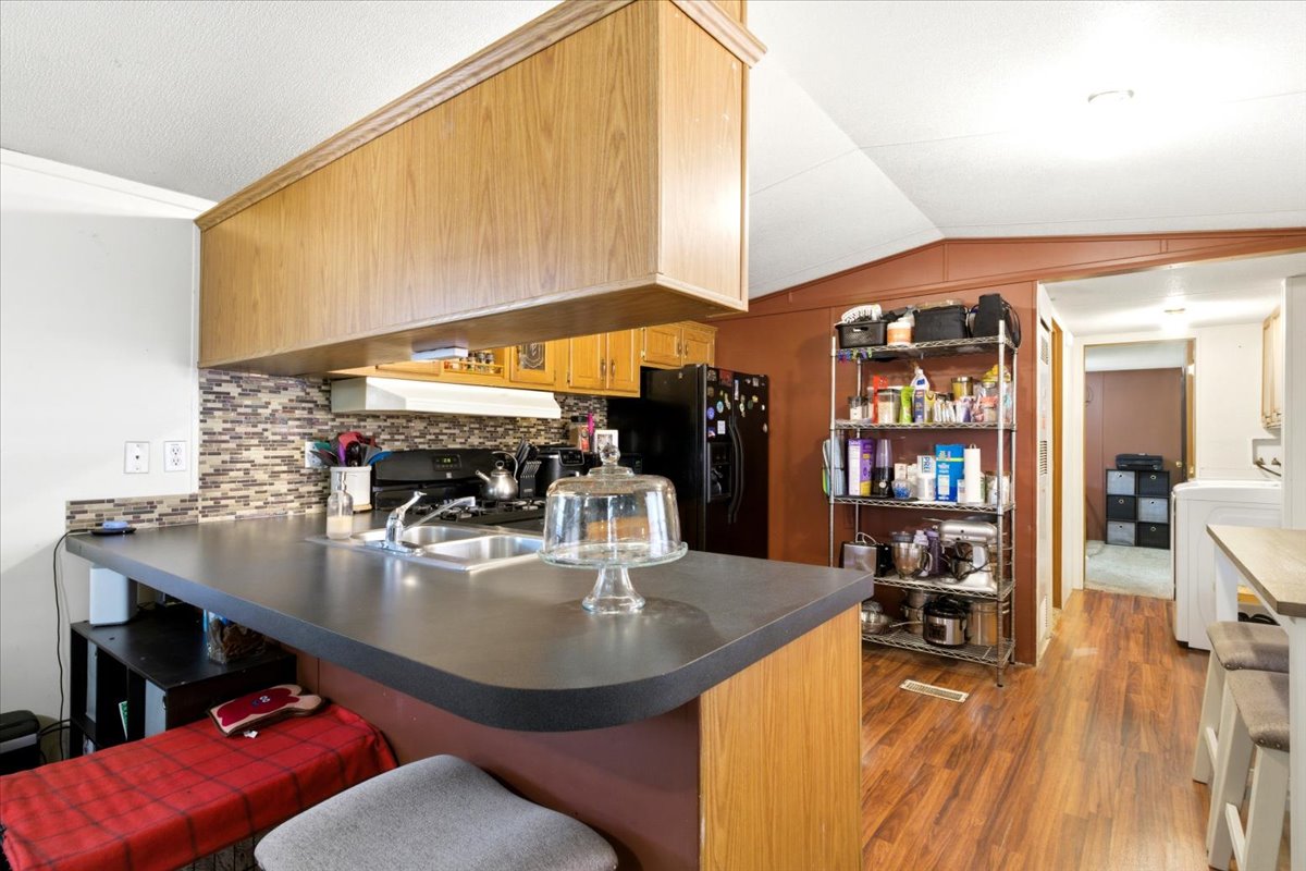 Kitchen featuring wood-finish flooring, a dark countertop peninsula with an integrated sink, and a mosaic tile backsplash