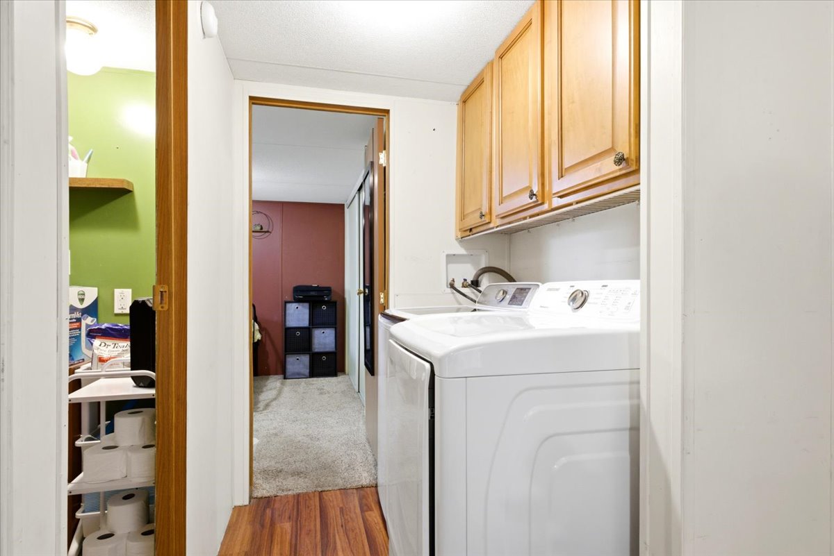 Dedicated laundry area featuring wood-finish flooring and upper cabinetry with dark hardware