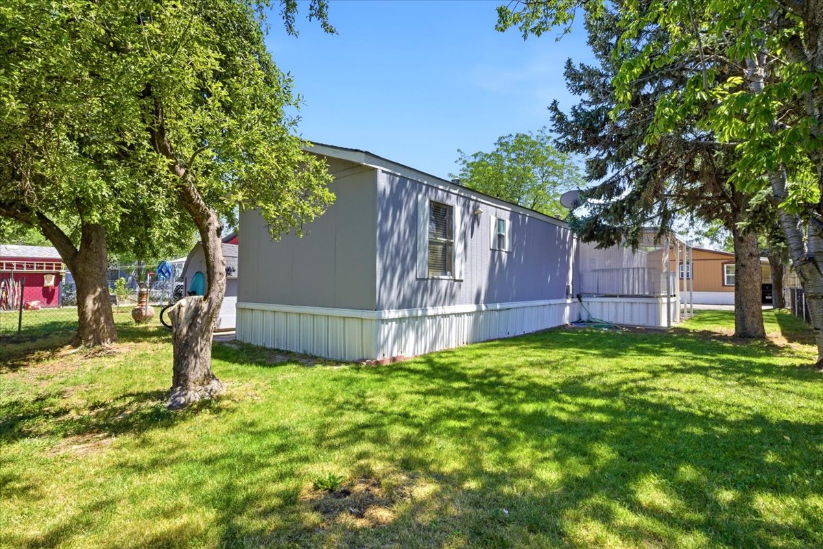 Manicured lawn with mature trees and a gray-sided home featuring white trim and skirting