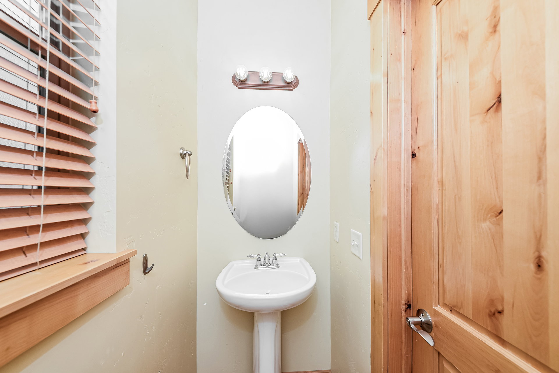 Pedestal sink with chrome faucet, illuminated by a three-light vanity fixture