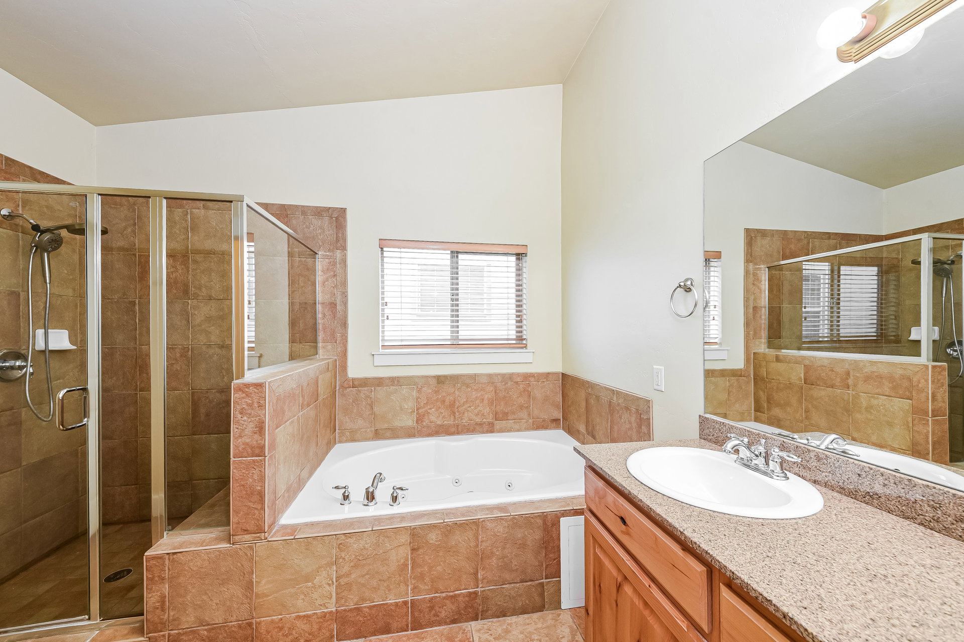 Bathroom featuring a large soaking tub, glass-enclosed shower with a handheld fixture, and a single vanity with a solid surface countertop