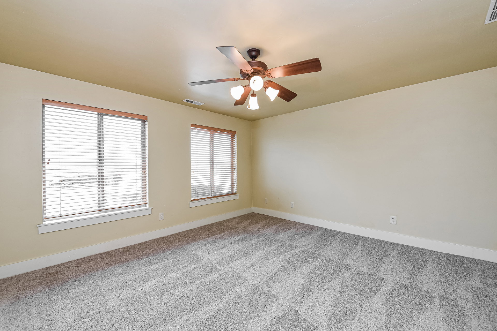 Spacious room featuring neutral-toned walls, patterned carpeting, and two windows with blinds
