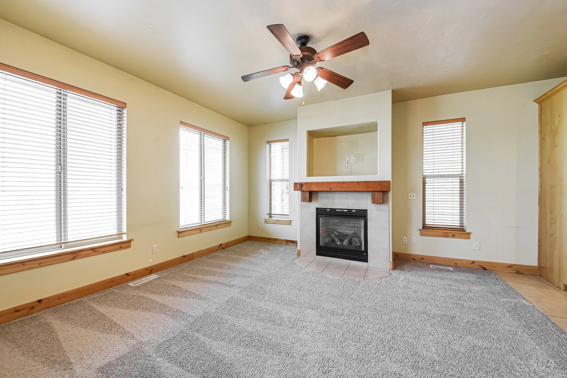 Living space featuring a tile-surround corner fireplace with wood mantel, built-in shelving, and a ceiling fan
