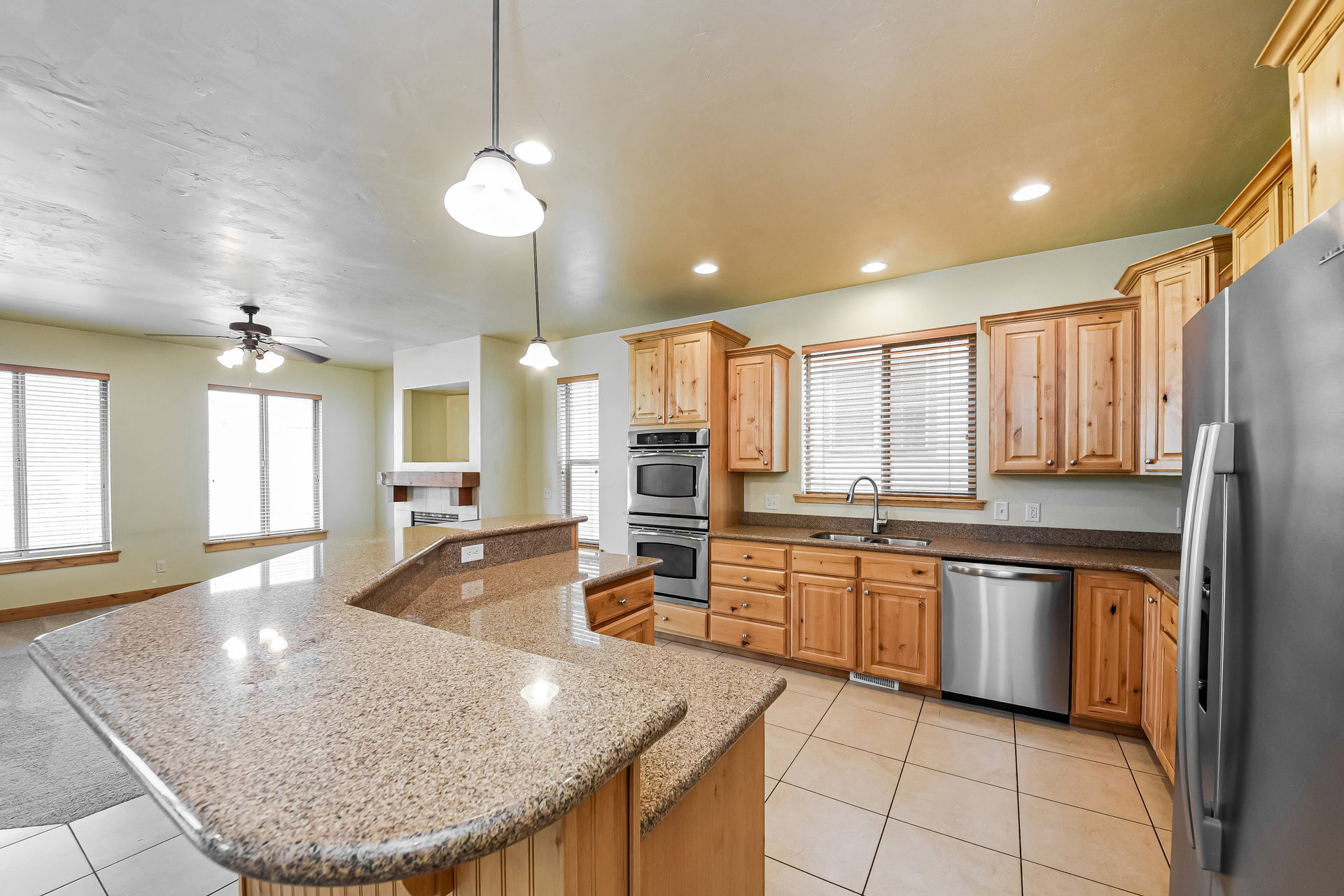 Kitchen featuring light wood cabinetry, granite-style countertops, stainless steel appliances including double ovens and a dishwasher, and a curved breakfast bar