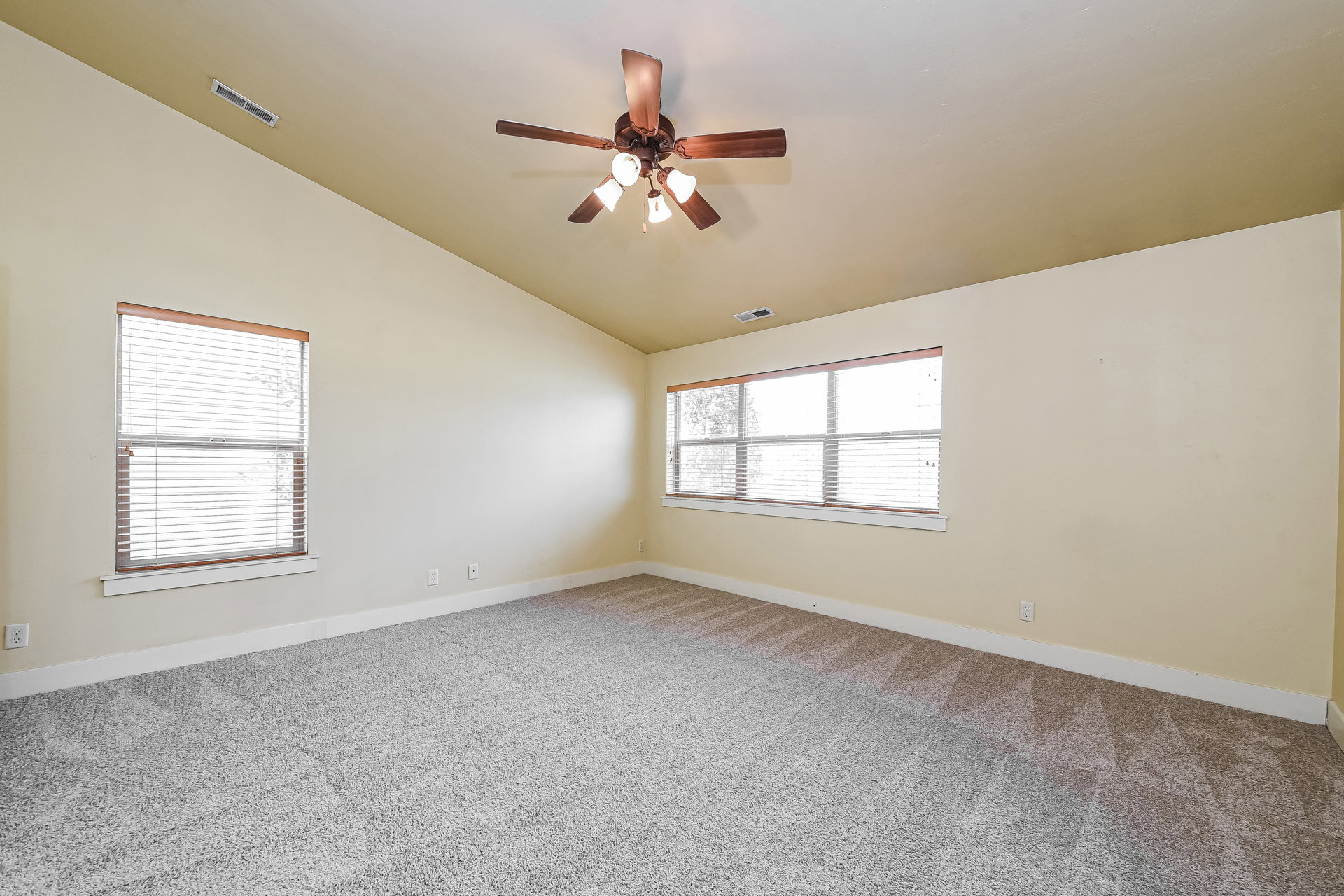 Spacious room featuring vaulted ceilings, a ceiling fan with integrated lighting, and light-colored carpeting