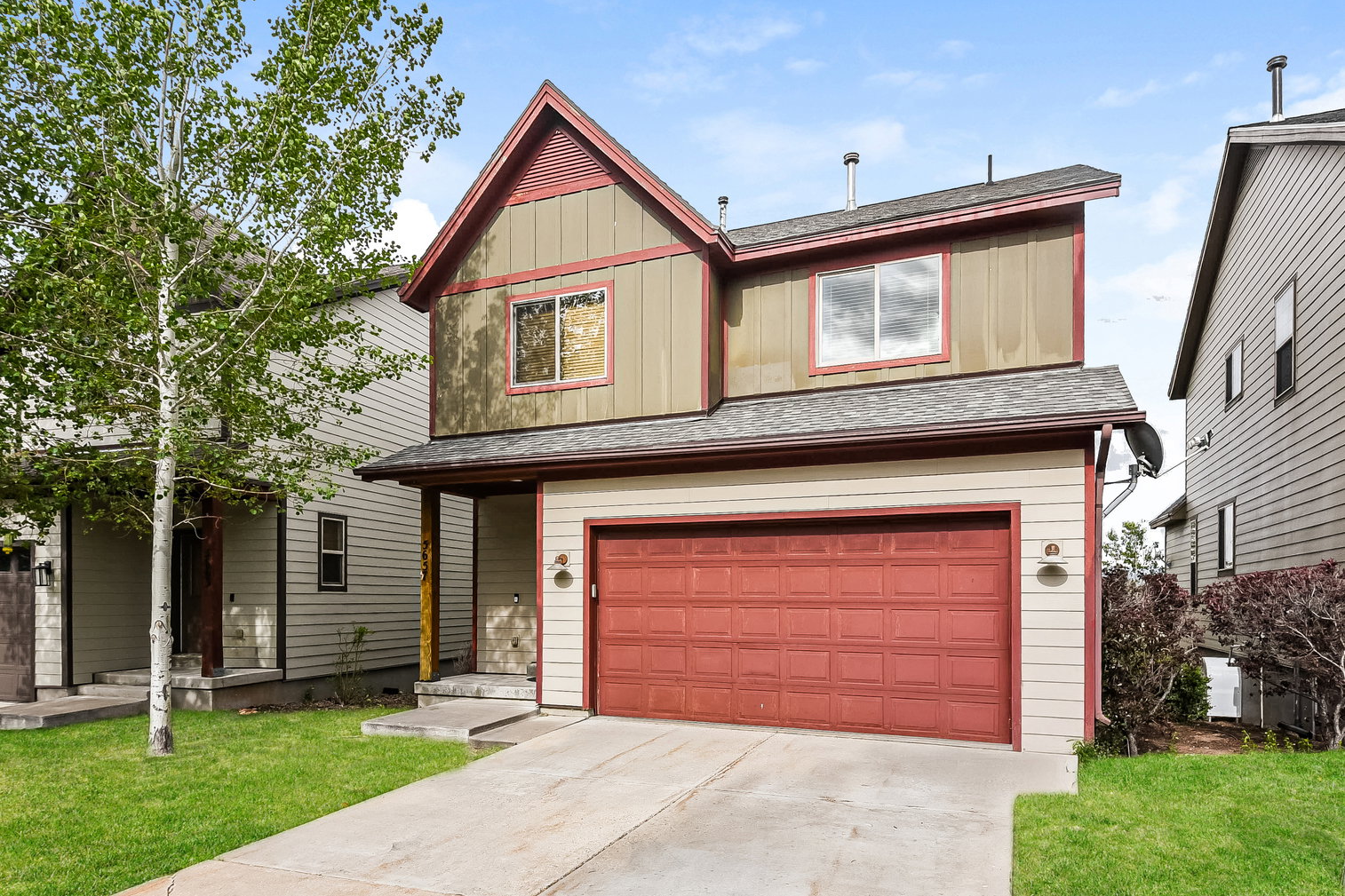 Two-story residence featuring a two-tone exterior with horizontal siding and vertical paneling, a prominent red garage door, and a concrete driveway