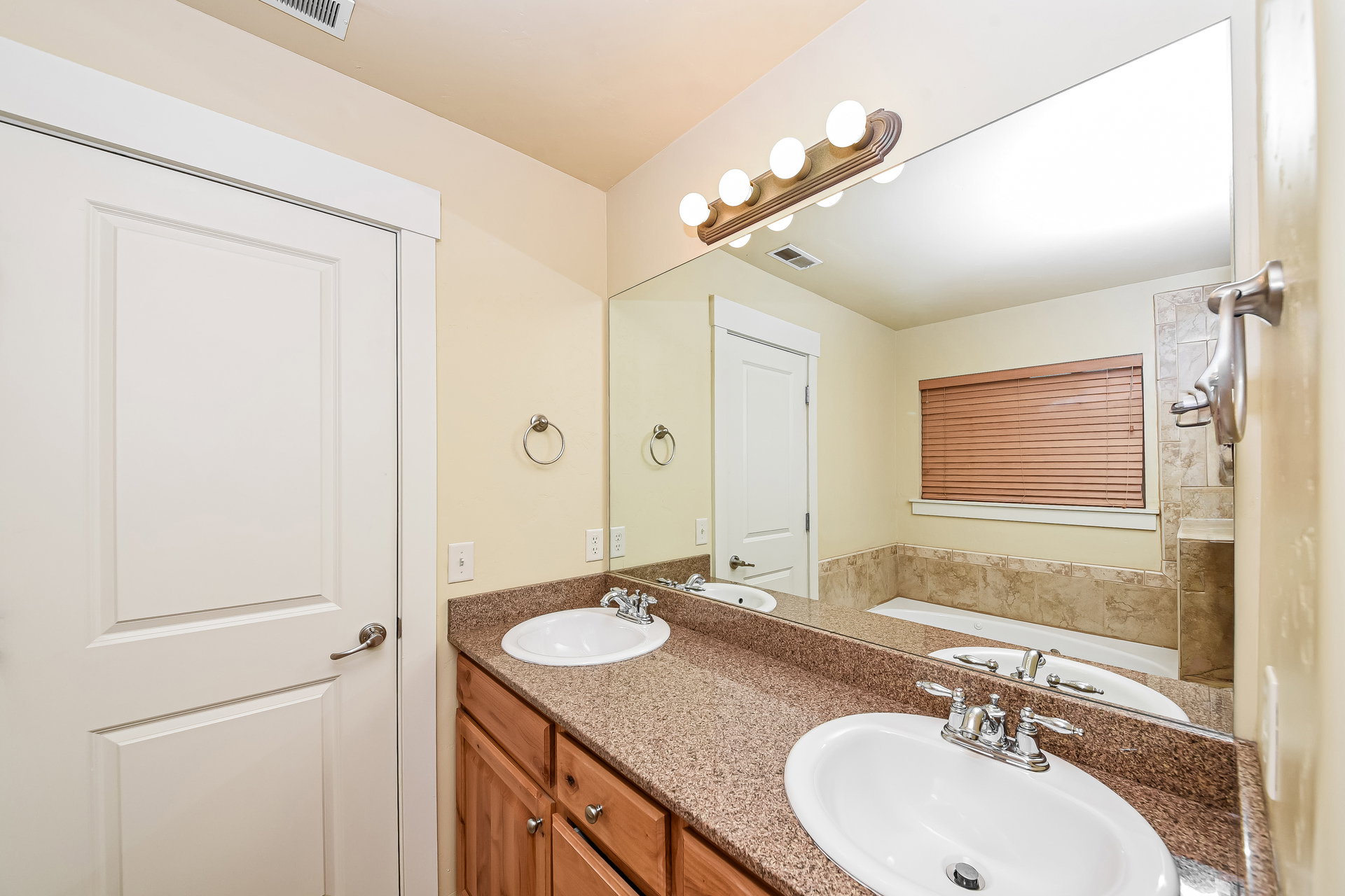 Dual vanity with granite-finish countertop, wood cabinetry, and chrome fixtures