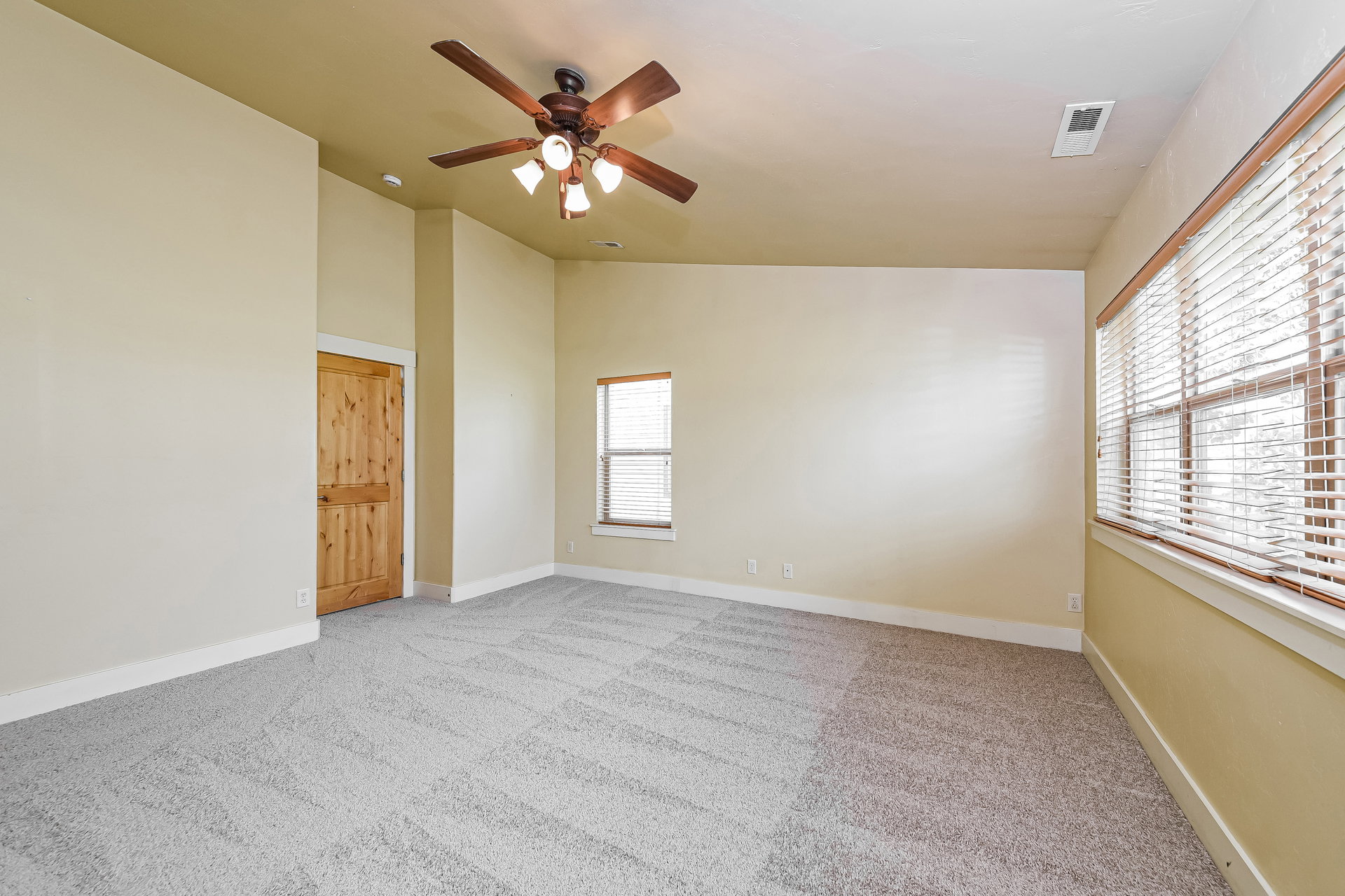 Spacious room featuring light-colored walls and patterned gray carpeting