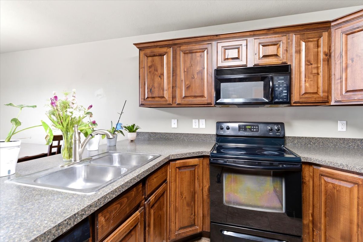 Kitchen featuring wood-finish cabinetry, a double basin stainless steel sink with a gooseneck faucet, an electric range, and a built-in microwave