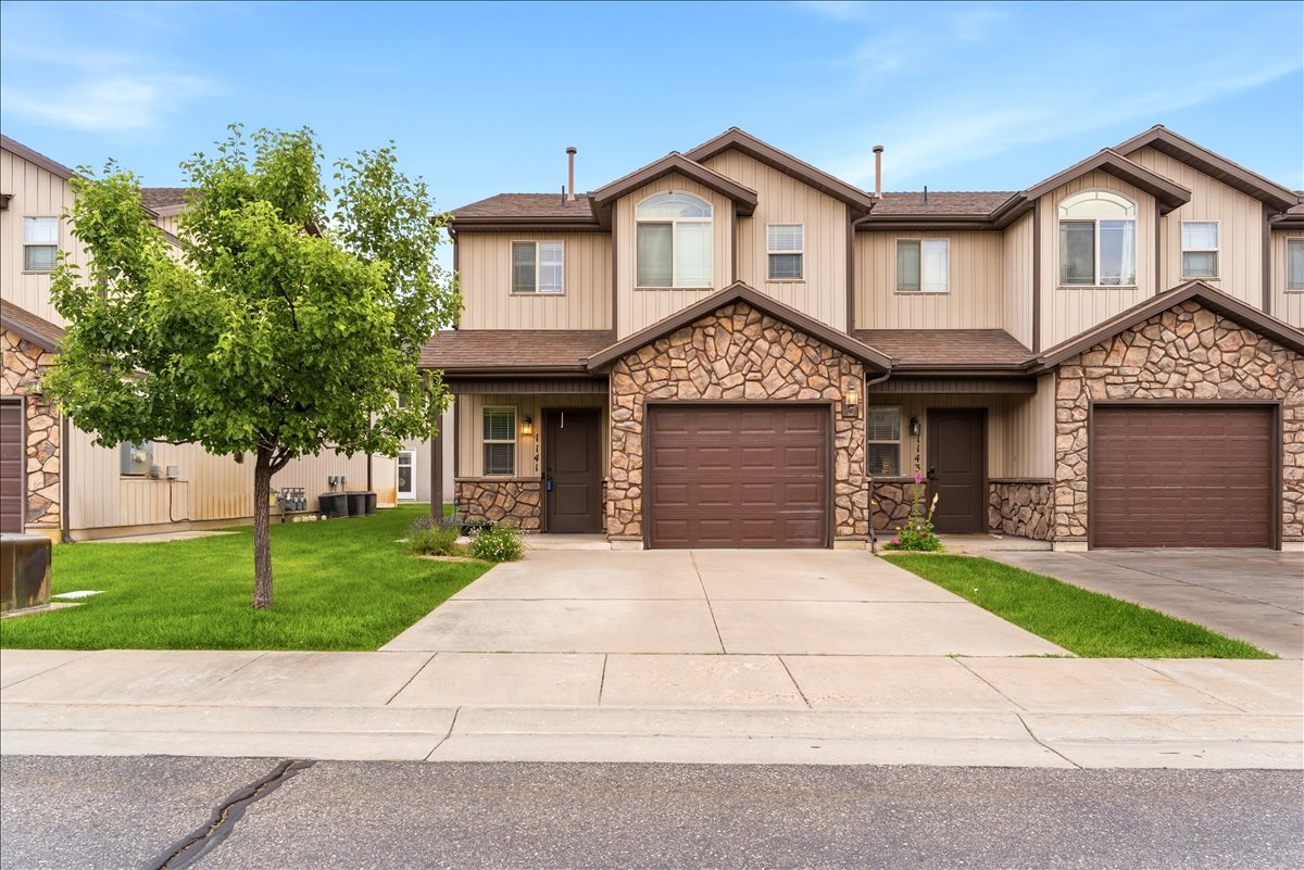 Townhome exterior featuring stacked stone accents, vertical siding, a pitched roof, and an attached garage with a brown door
