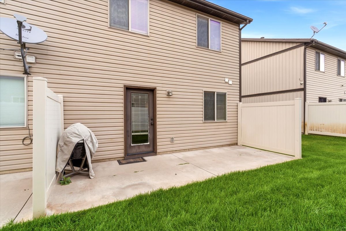 Rear concrete patio with direct access to interior, surrounded by a manicured lawn and privacy fencing