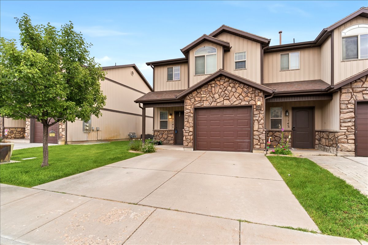 Townhome exterior featuring stone veneer accents, an integrated garage, and a covered entry