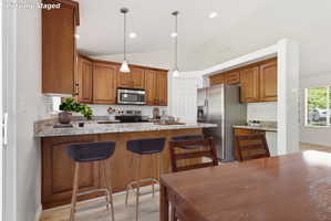 Kitchen featuring warm wood cabinetry, light-toned countertops, stainless steel appliances, and a breakfast bar