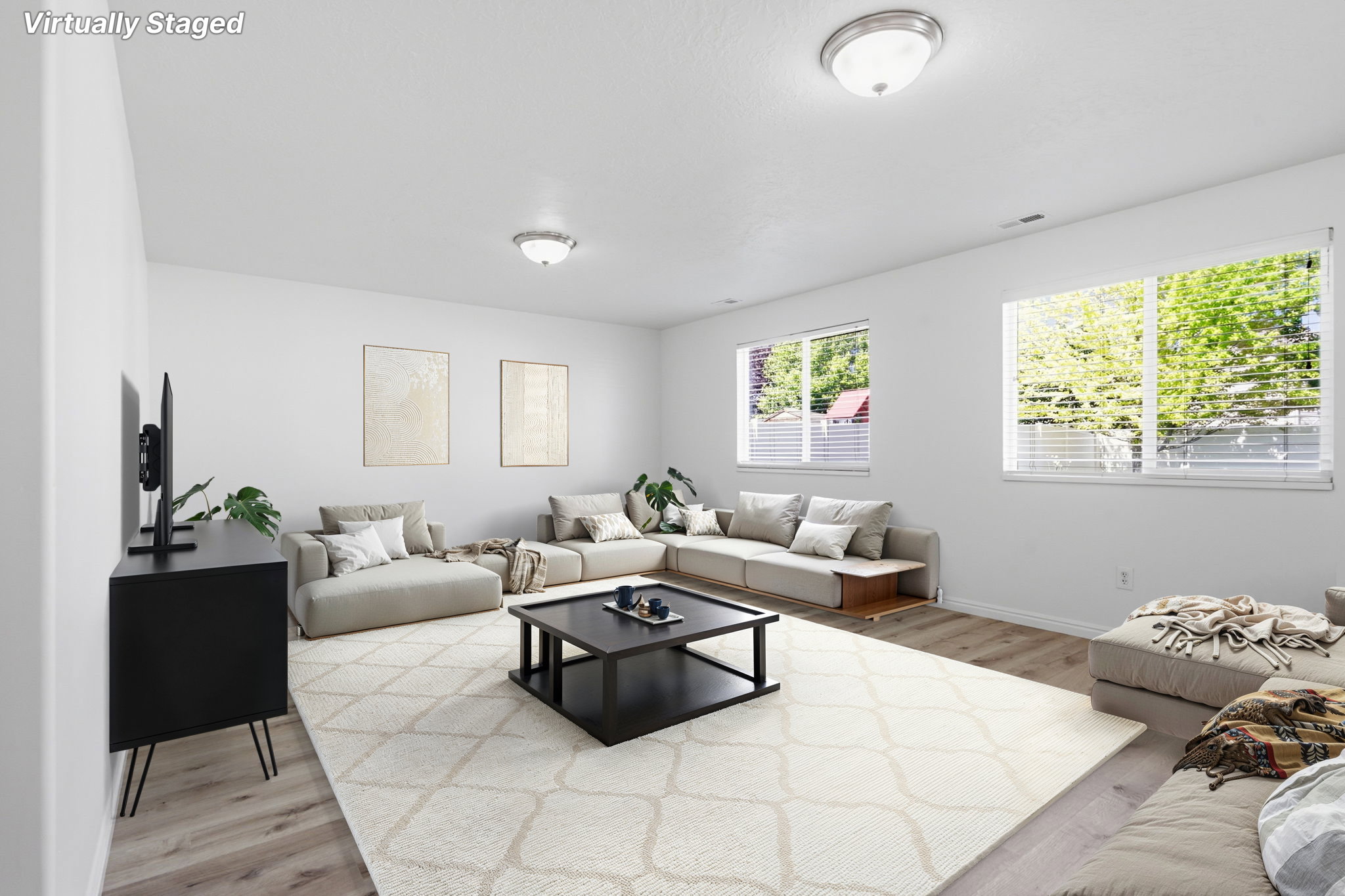 Spacious living area featuring light wood-finish flooring and multiple windows with horizontal blinds