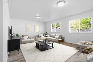 Spacious living area featuring light wood-finish flooring and multiple windows with horizontal blinds