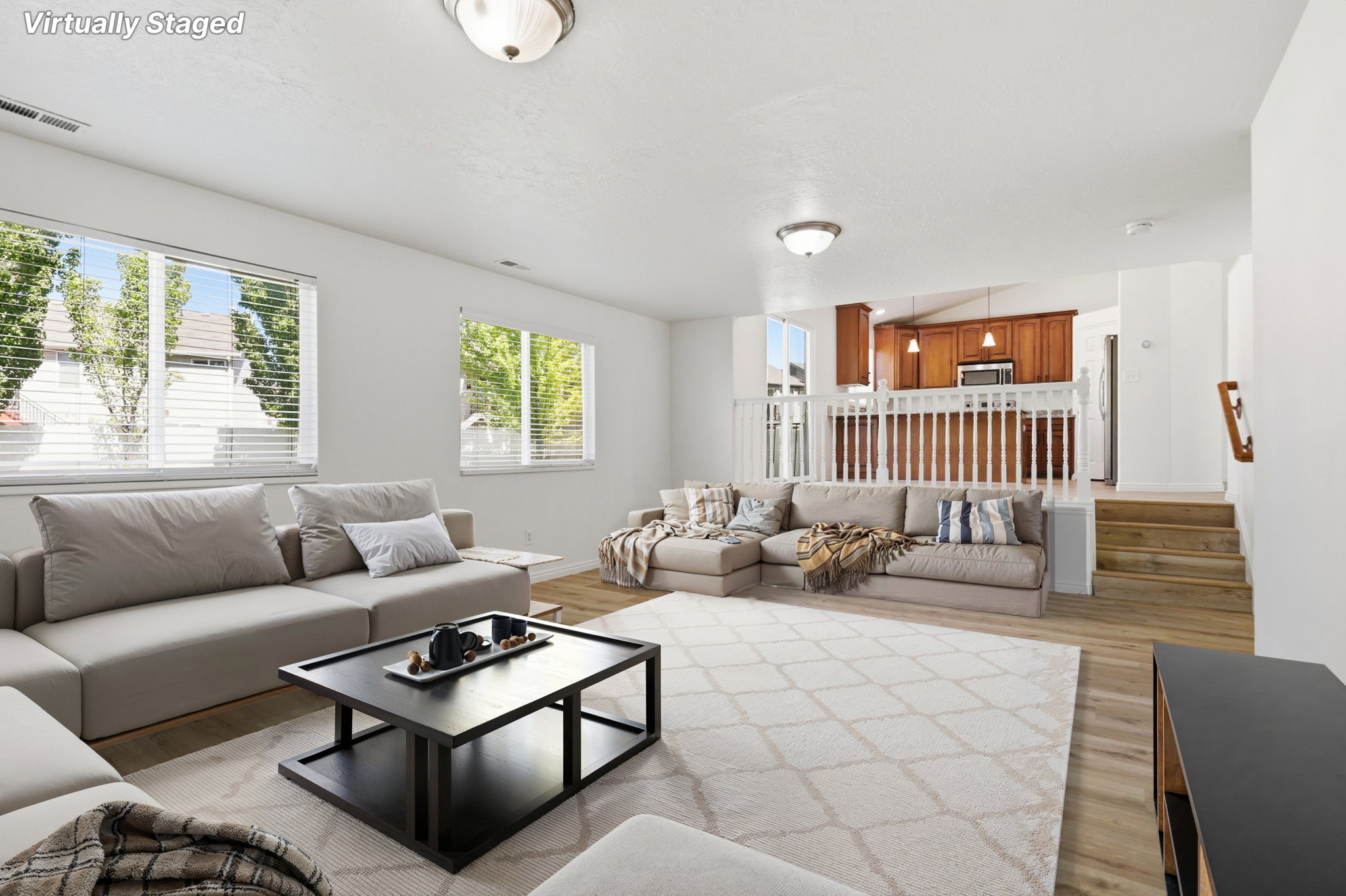 Spacious living area featuring light-toned flooring, multiple windows with blinds, and recessed lighting