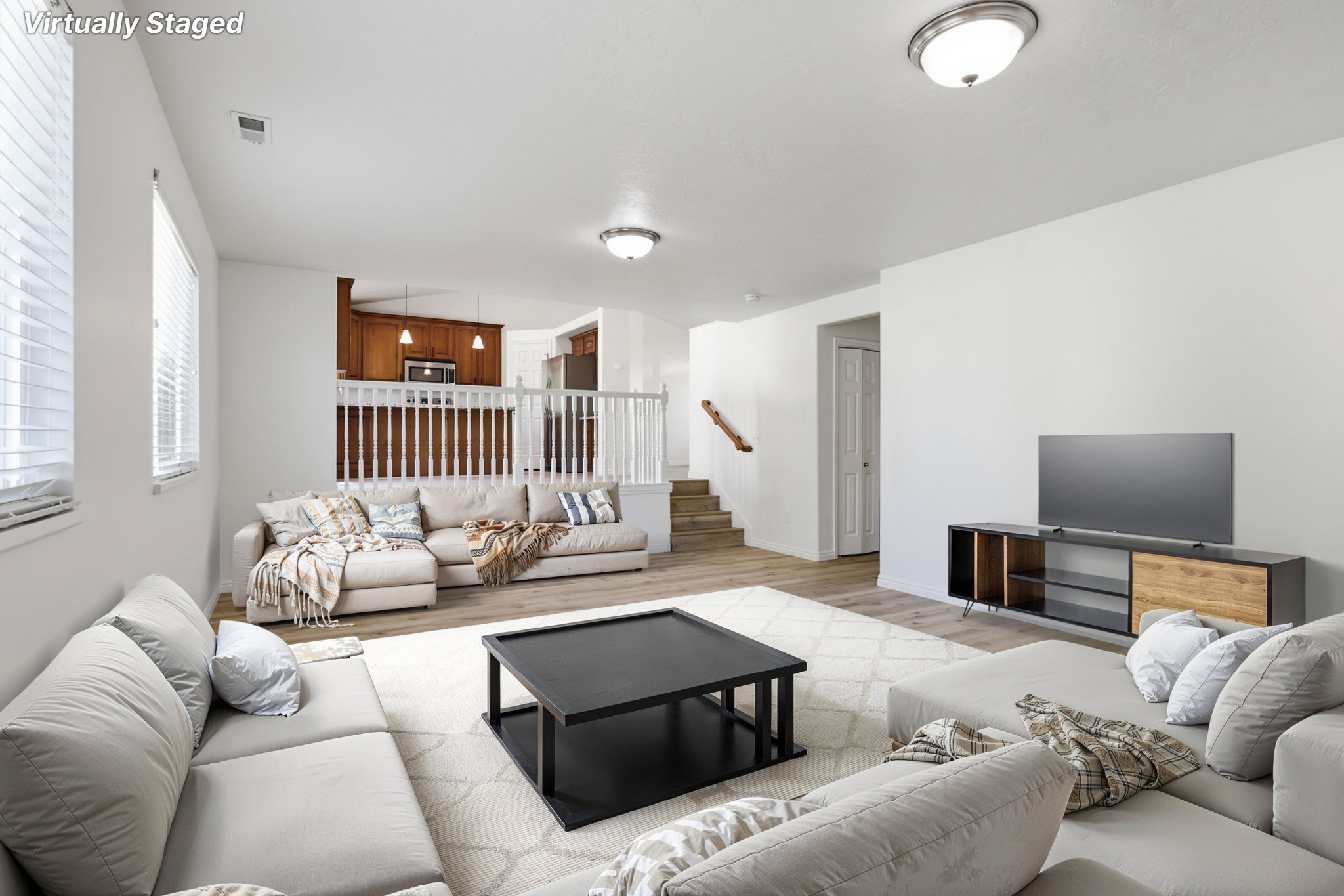 Spacious living area featuring light wood-finish flooring, white walls, and multiple windows