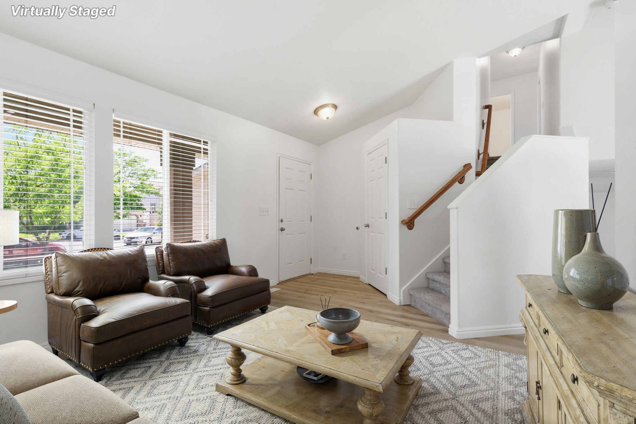 Bright living space featuring multiple windows with blinds, wood-finish flooring, a carpeted staircase with a wood handrail, and white interior doors