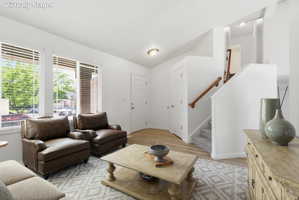 Bright living space featuring multiple windows with blinds, wood-finish flooring, a carpeted staircase with a wood handrail, and white interior doors