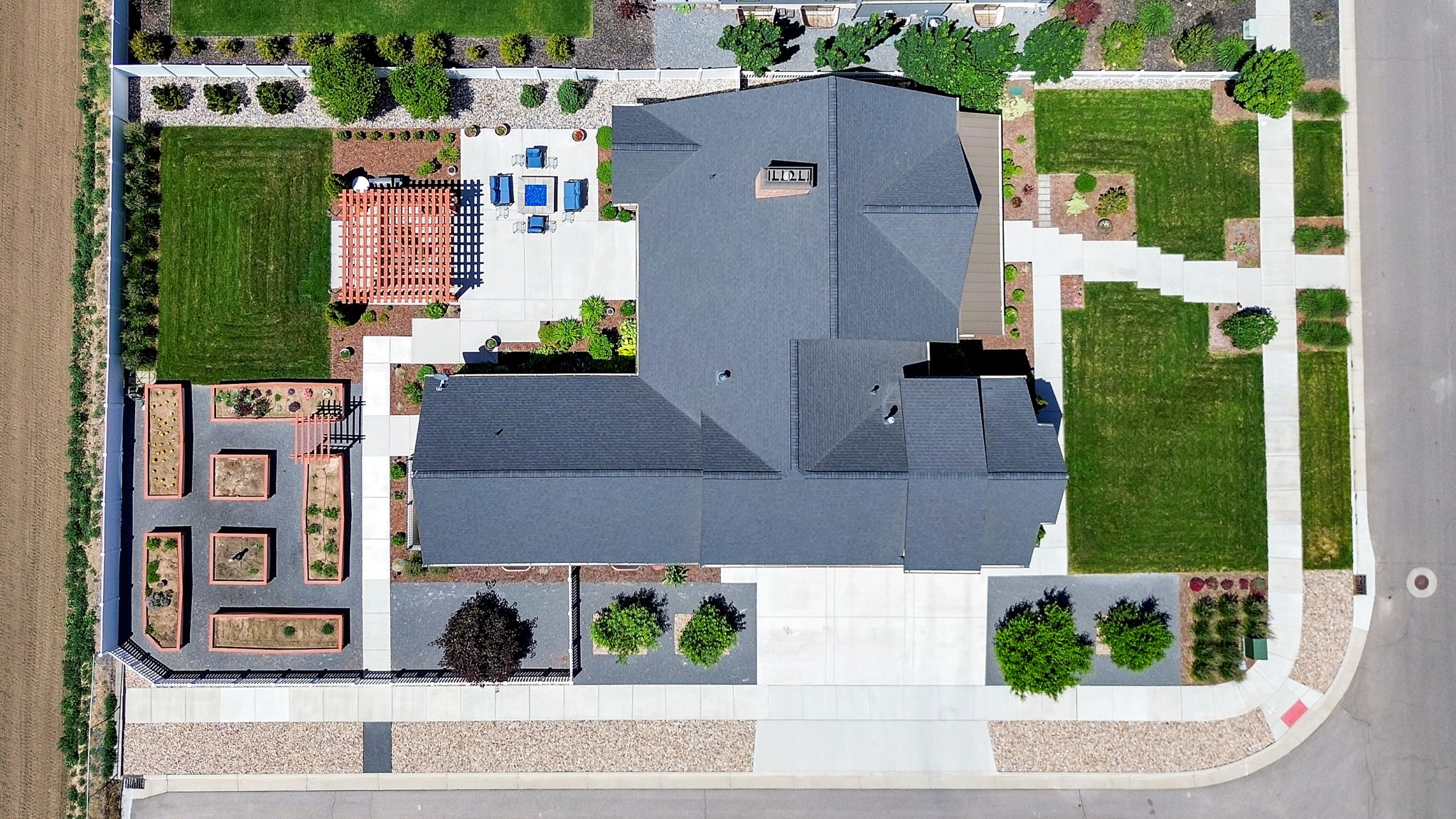 Expansive property featuring a multi-gabled roofline, concrete patio, a wooden pergola, manicured lawns, and raised garden beds