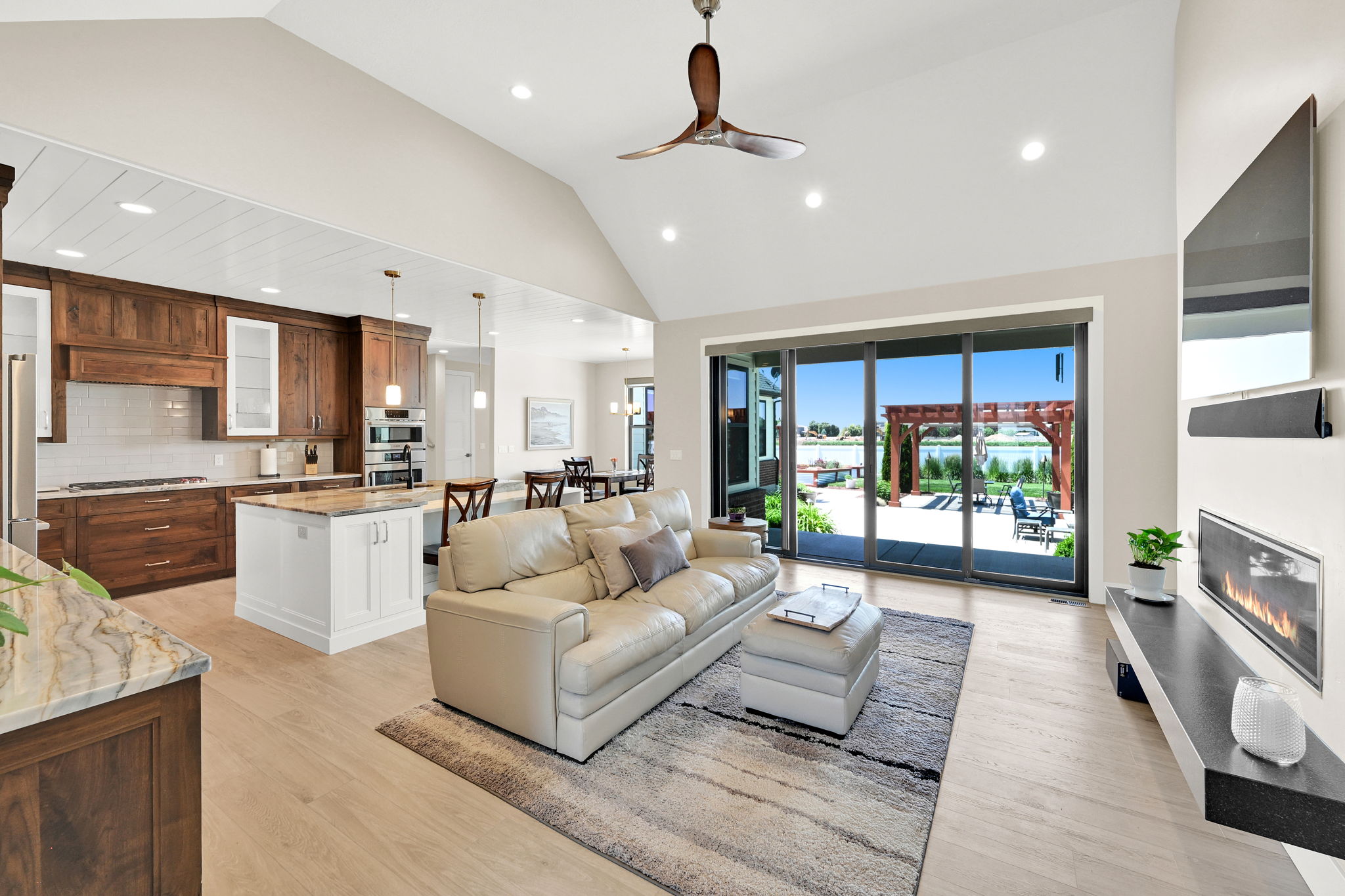 Open-concept living area featuring a vaulted ceiling with recessed lighting and a ceiling fan, light wood-finish flooring, and a linear gas fireplace