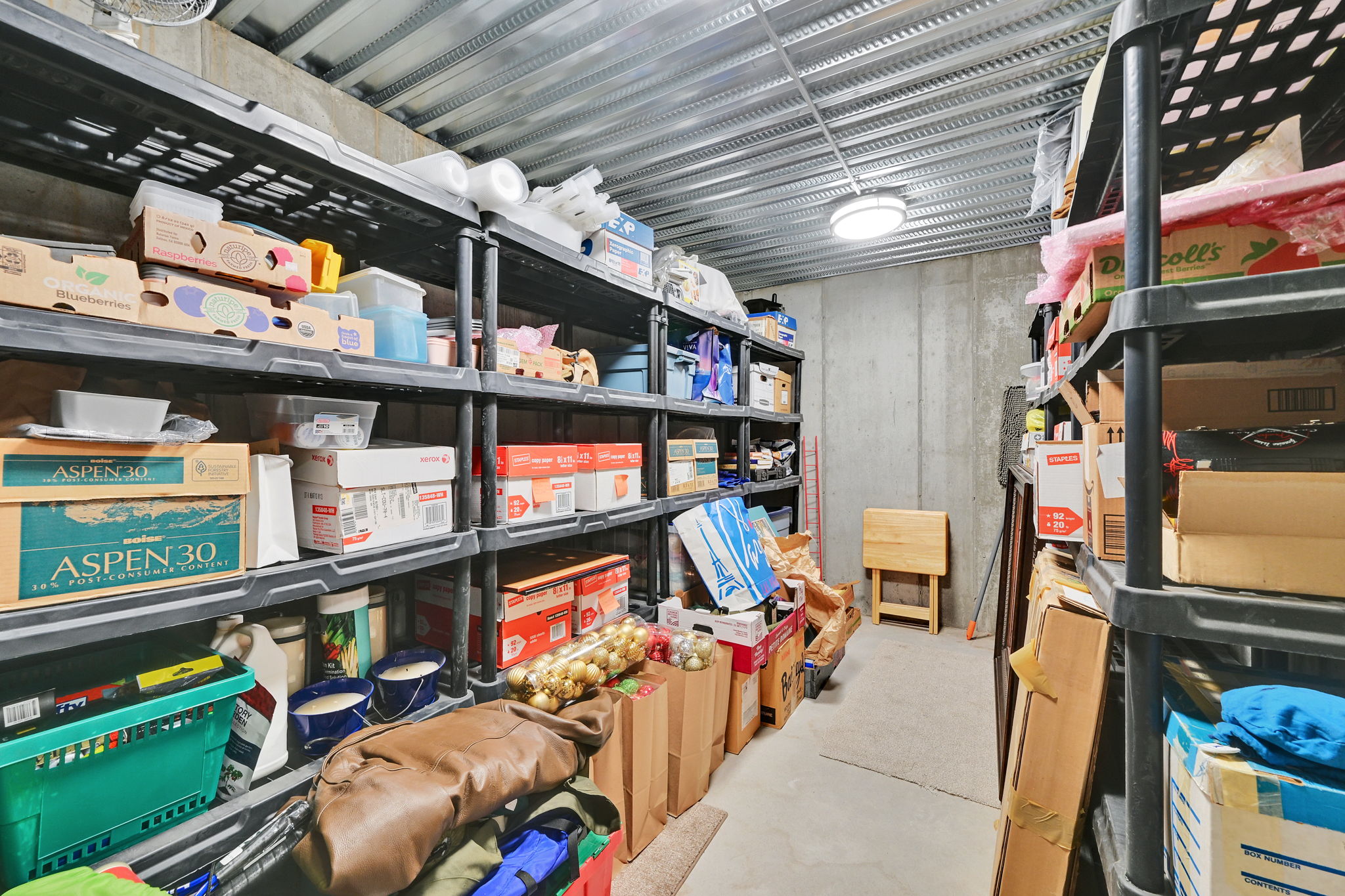 Dedicated storage area featuring concrete walls, a corrugated metal ceiling, and overhead lighting