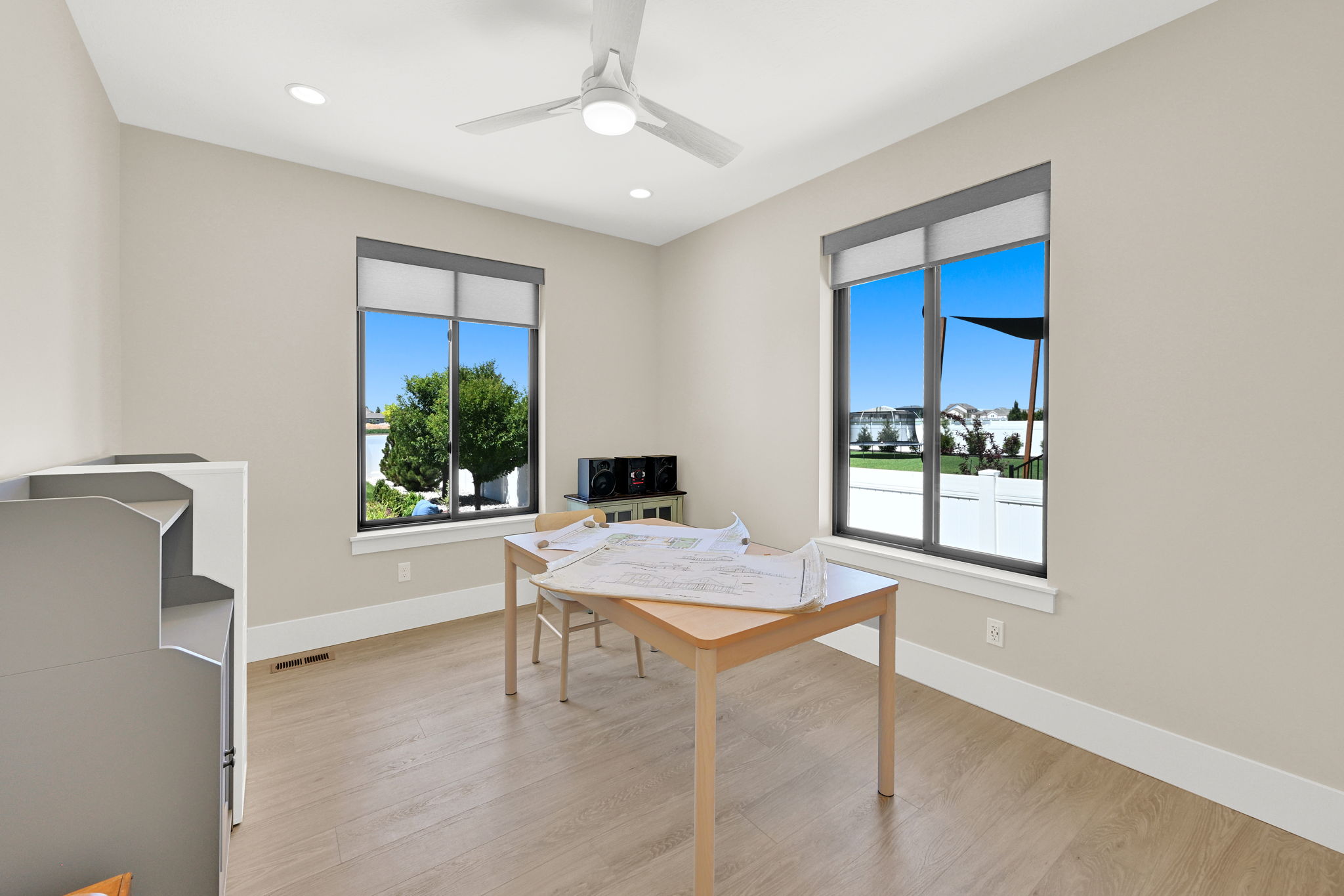 Bright interior space featuring two large windows with dark frames, wood-finish flooring, and light neutral wall paint