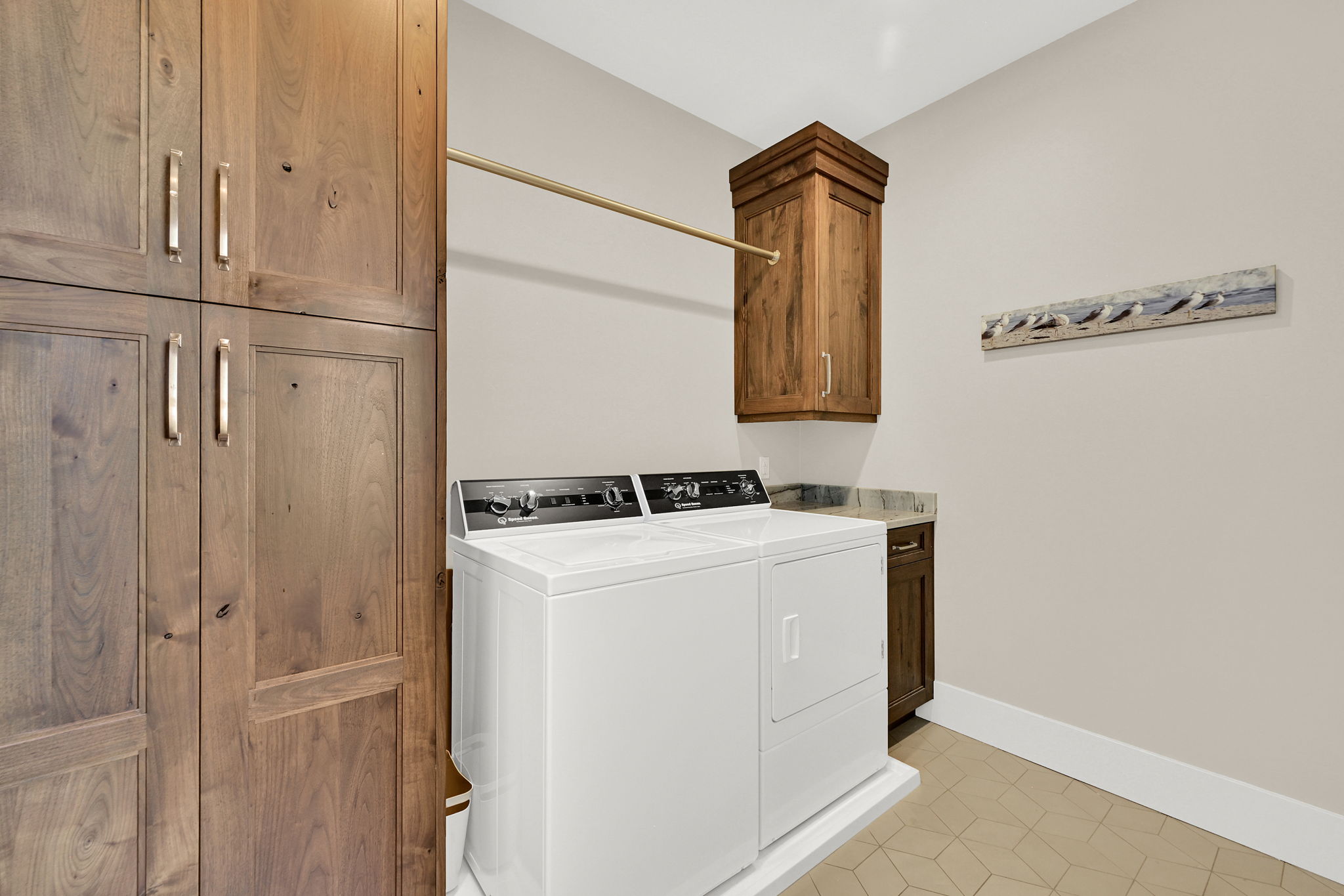 Laundry area featuring stacked white appliances, wood-finish cabinetry, and a gold-finish hanging rod