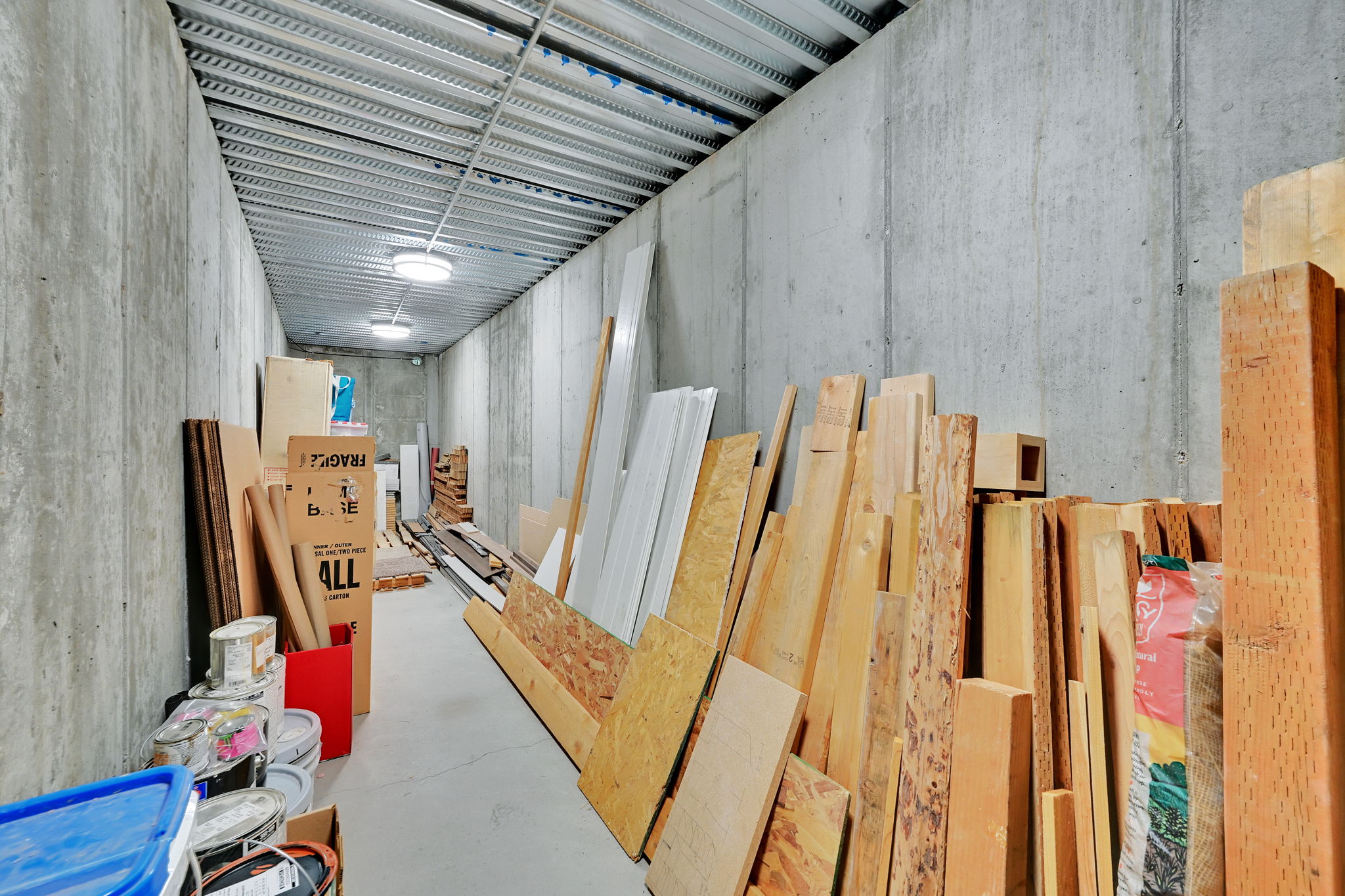 Concrete walled storage area with a corrugated metal ceiling and flush-mounted ceiling lights