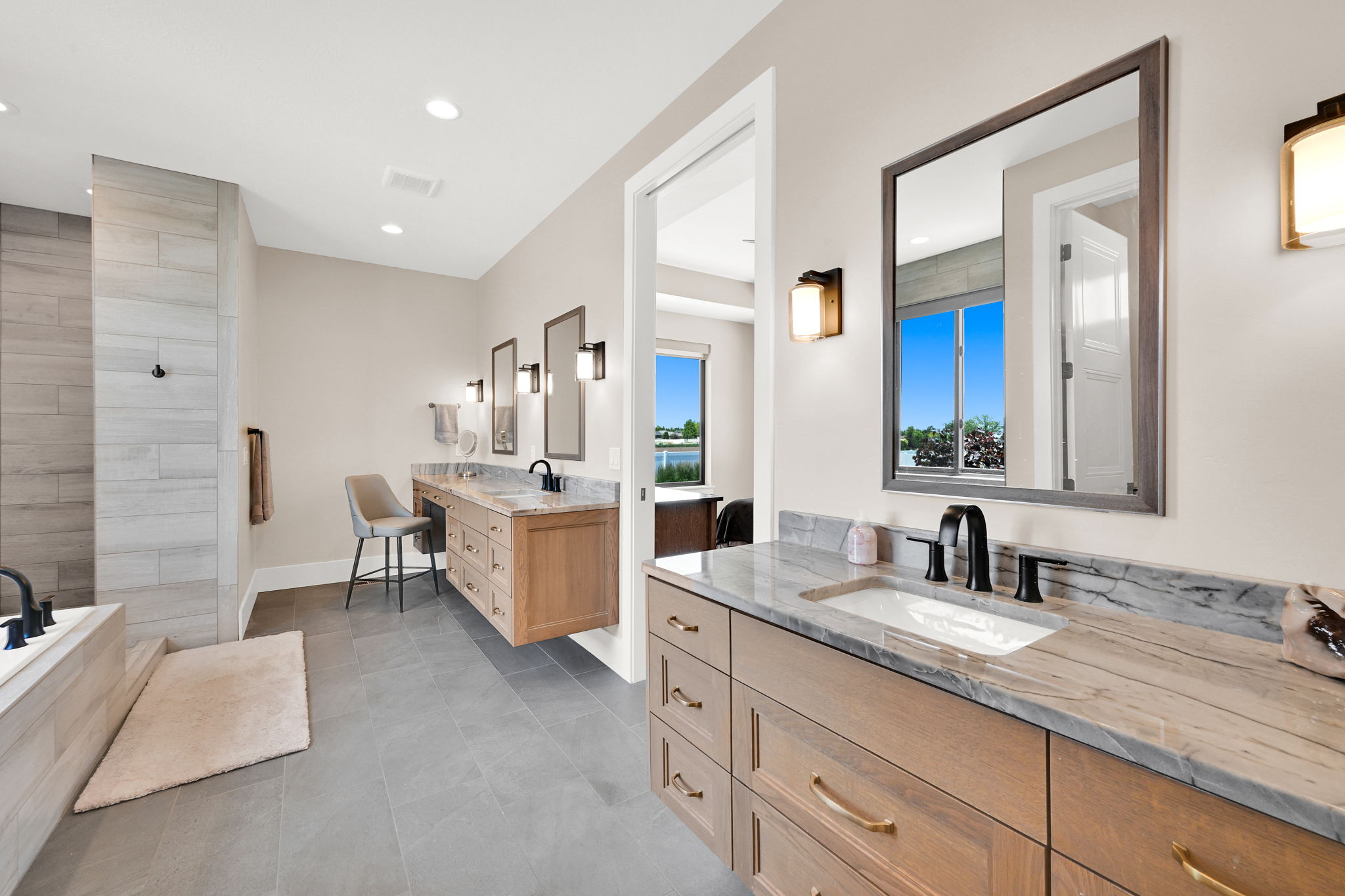 Spacious bathroom featuring dual floating wood-finish vanities with stone countertops, integrated sinks, and matte black fixtures