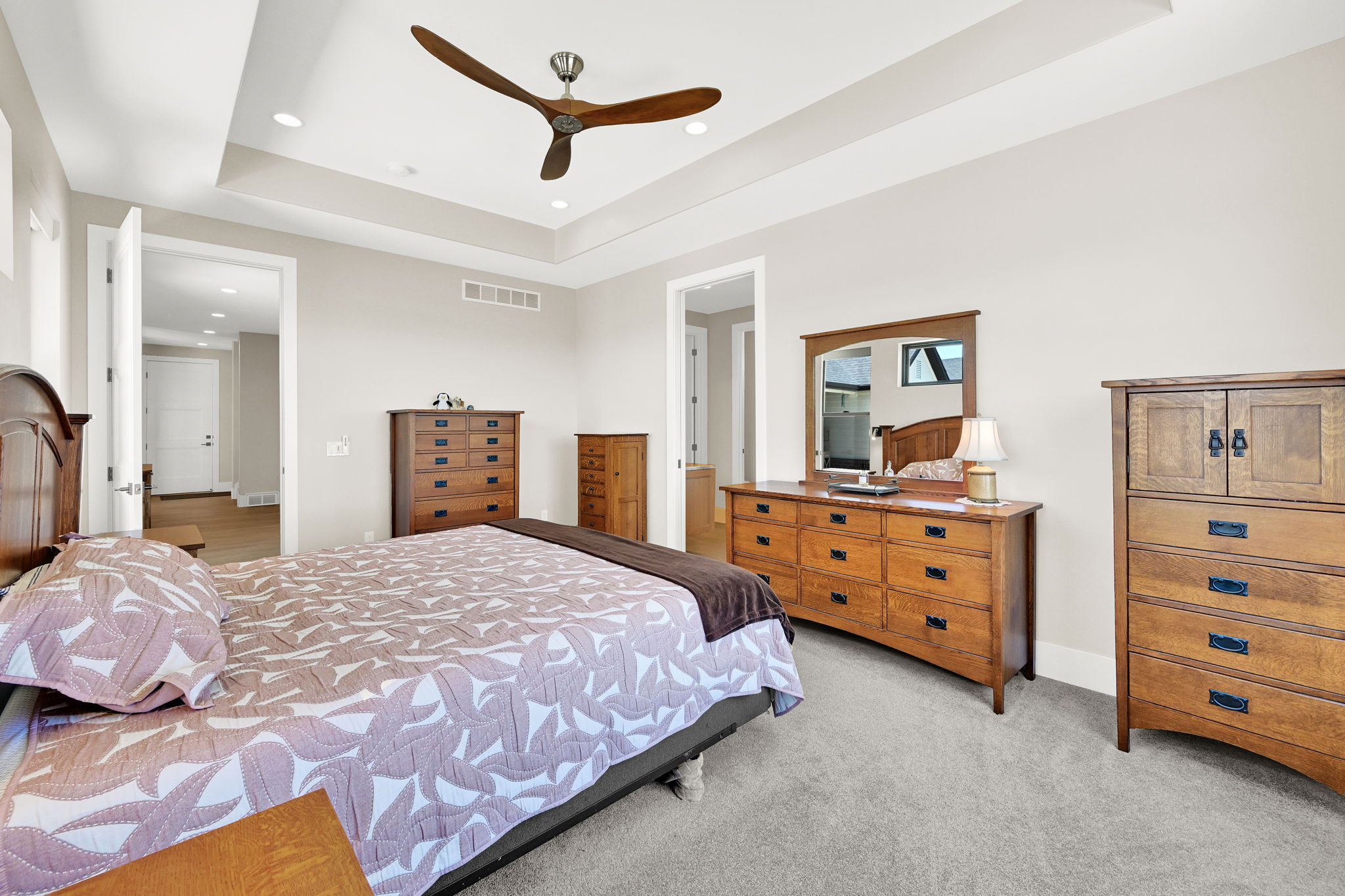 Recessed lighting, tray ceiling, and a contemporary ceiling fan complement the neutral wall tones and grey carpeting