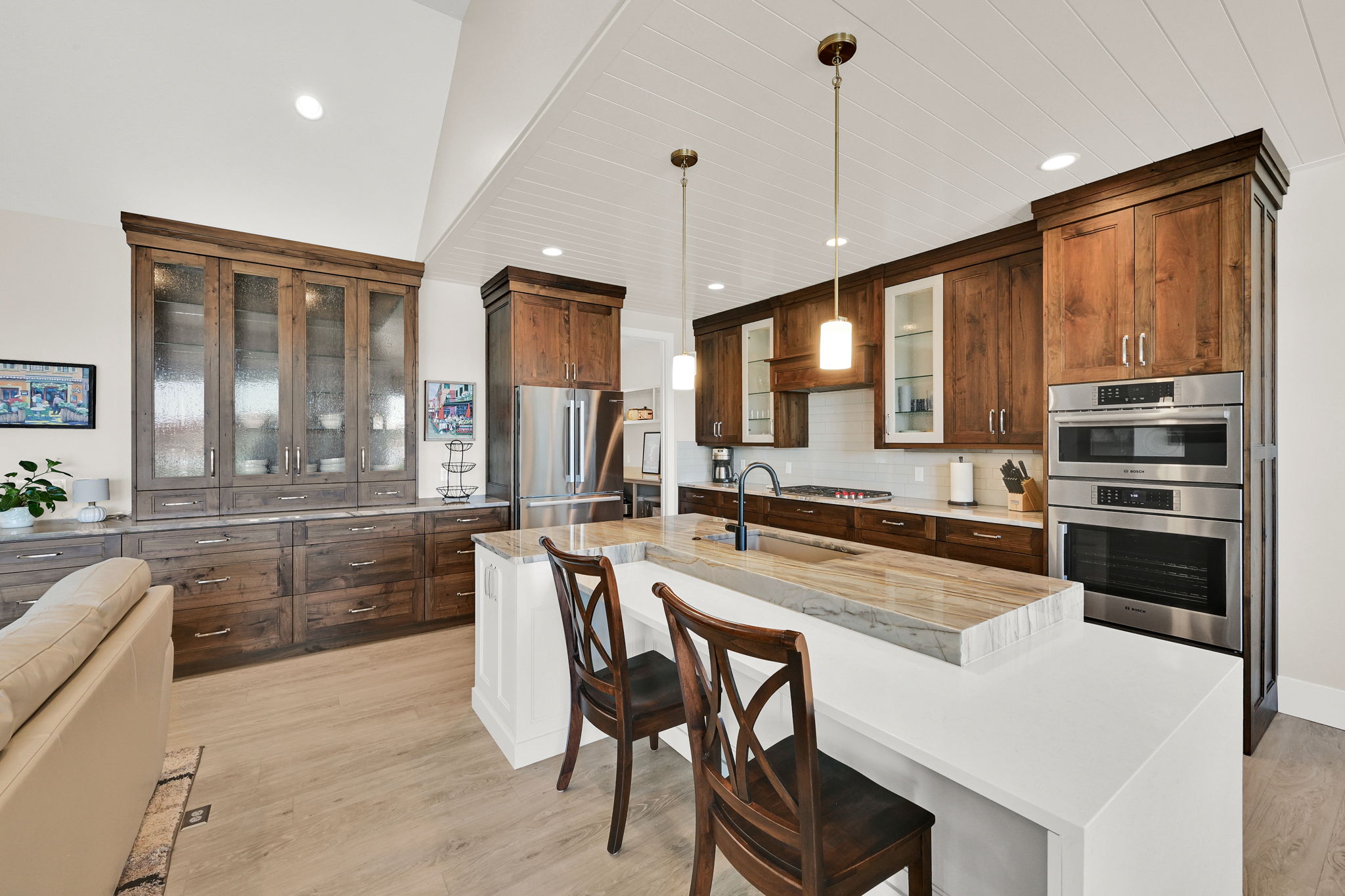 Open-concept kitchen featuring vaulted ceilings with shiplap, rich wood cabinetry, stainless steel double ovens, a large kitchen island with countertop seating, and wood-finish flooring