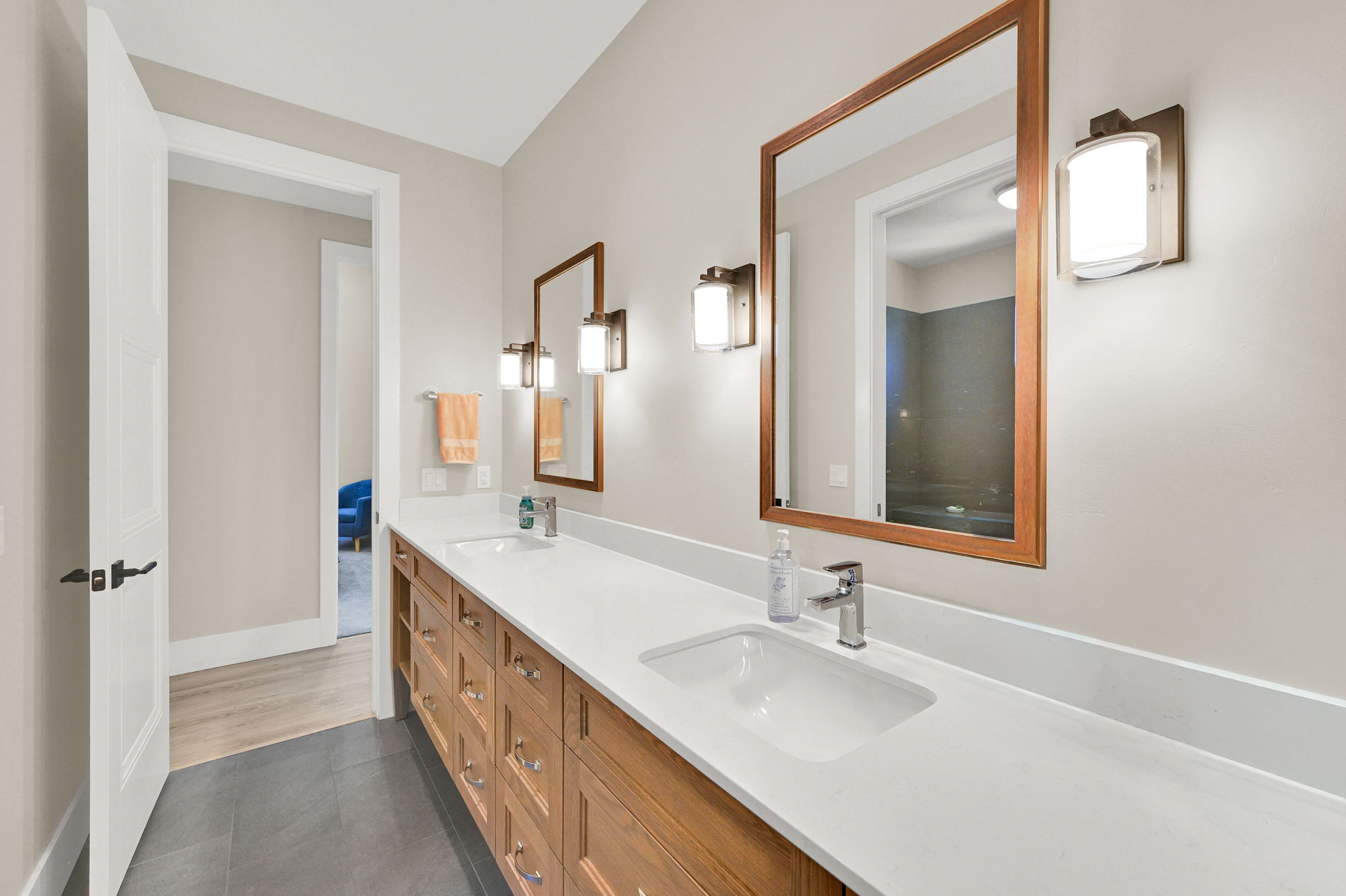 Dual vanity with white undermount sinks, expansive white countertop, and light wood-finish cabinetry featuring brass hardware