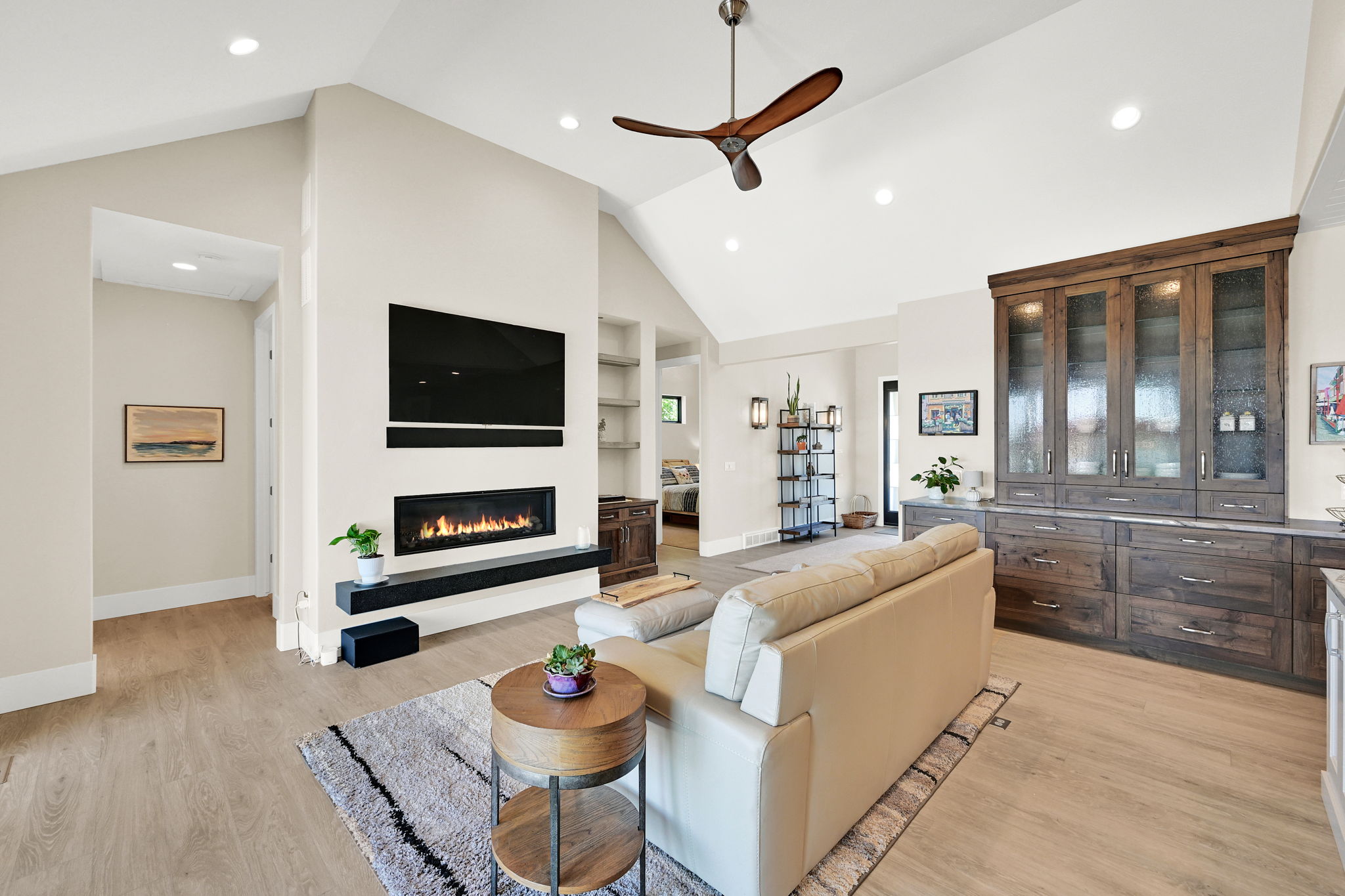 Vaulted ceilings with recessed lighting, linear fireplace, dark wood-finish built-in cabinetry with glass fronts, light wood-finish flooring, and a modern ceiling fan