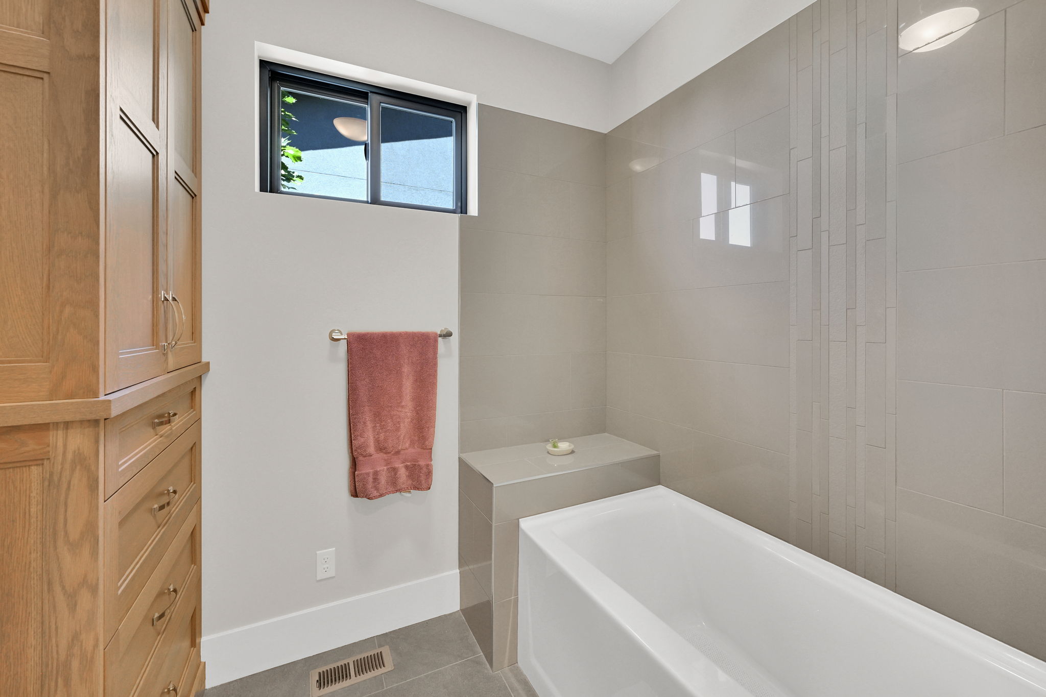 Bathtub with integrated bench seating, complemented by floor-to-ceiling tilework featuring a decorative vertical accent