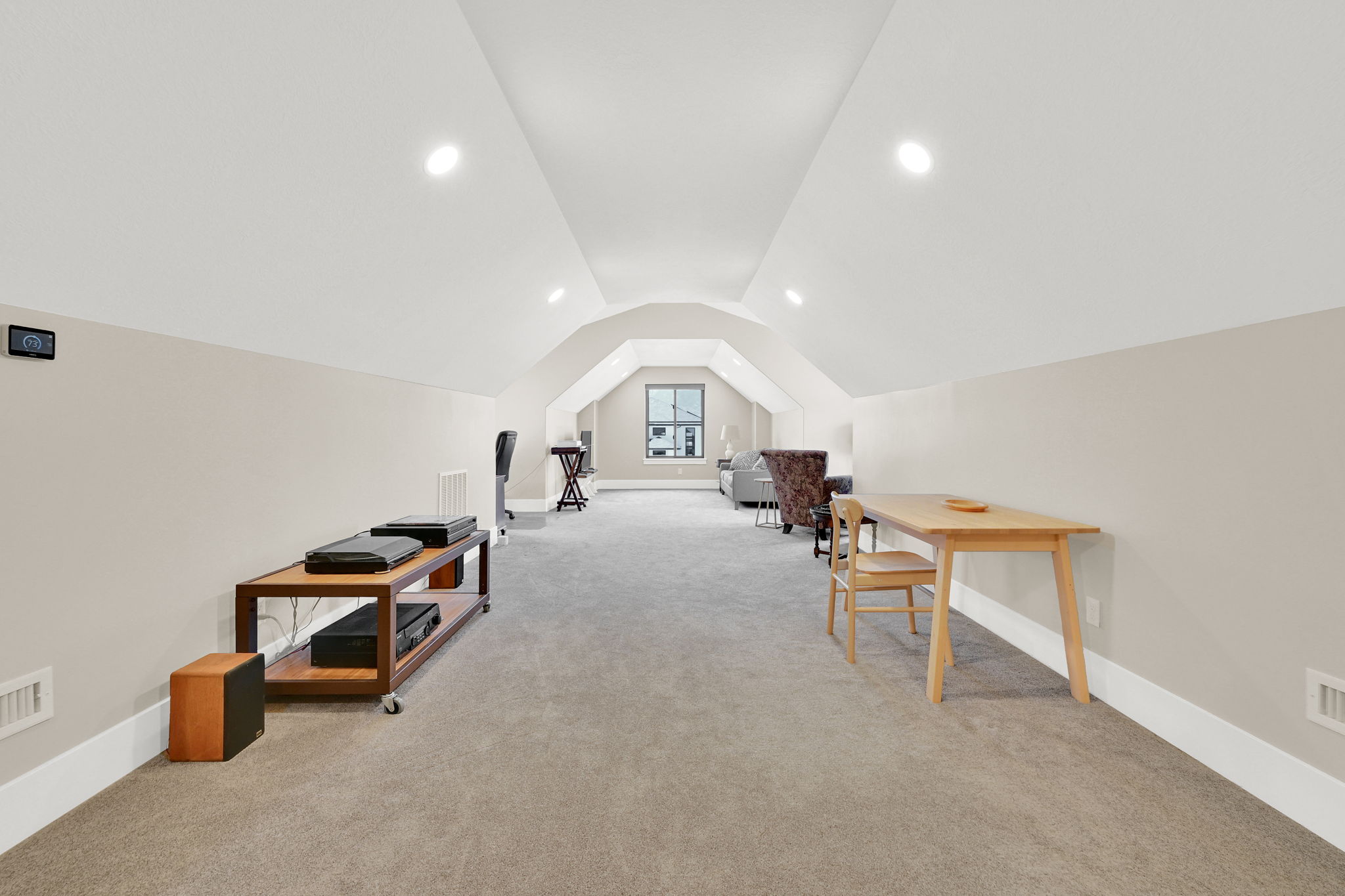 Spacious finished attic space featuring sloped ceilings, recessed lighting, neutral carpeting, and a window