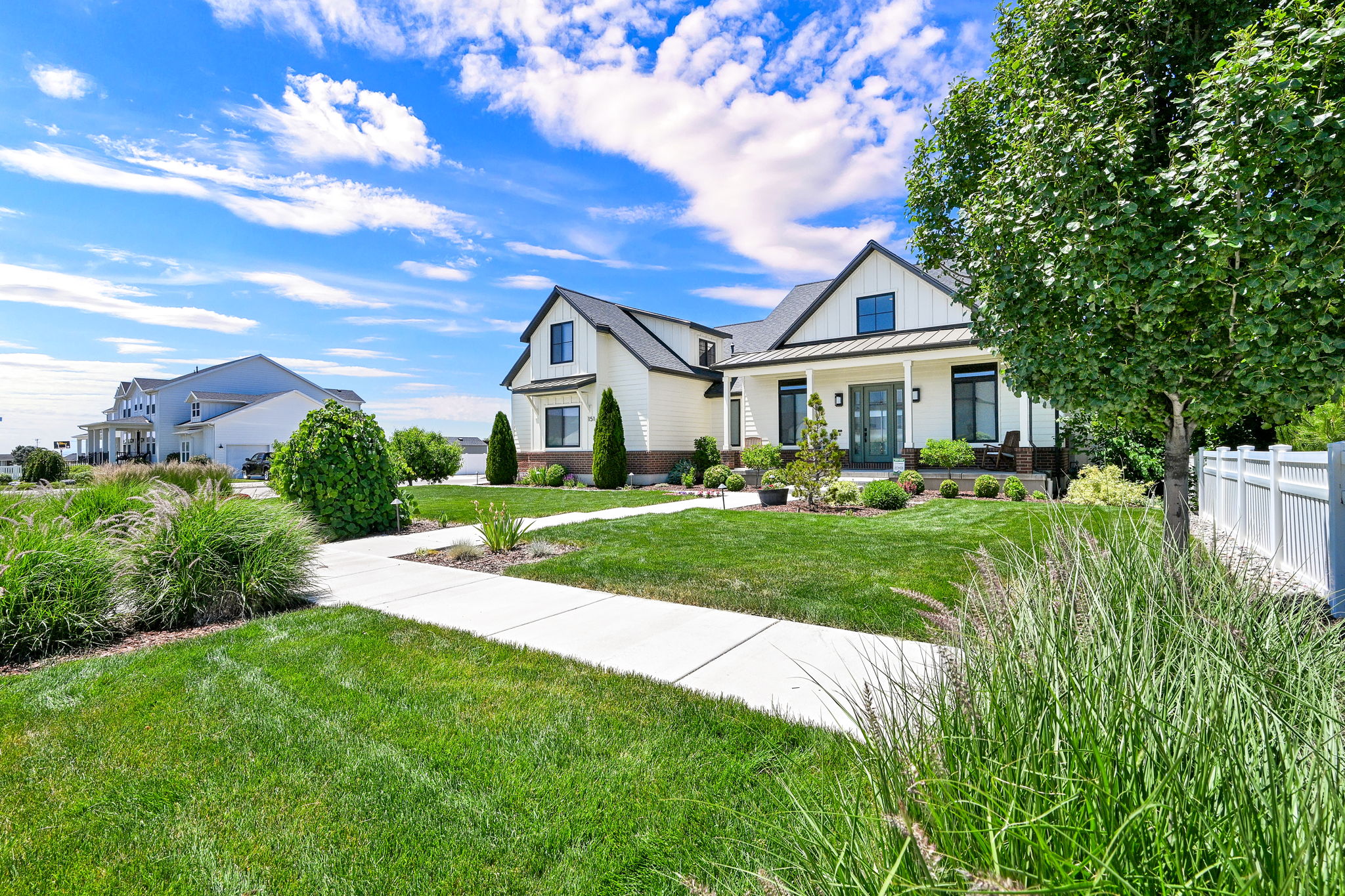 Modern farmhouse exterior with a covered porch, dark trim accents, a dark roof, and a white picket fence