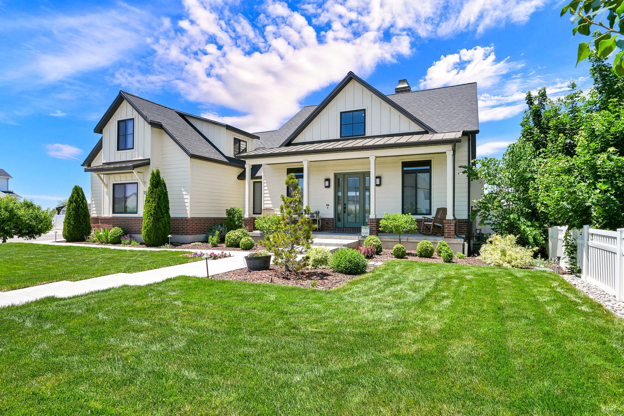 Modern farmhouse exterior featuring an inviting covered porch, dark roof, white siding, and a brick foundation