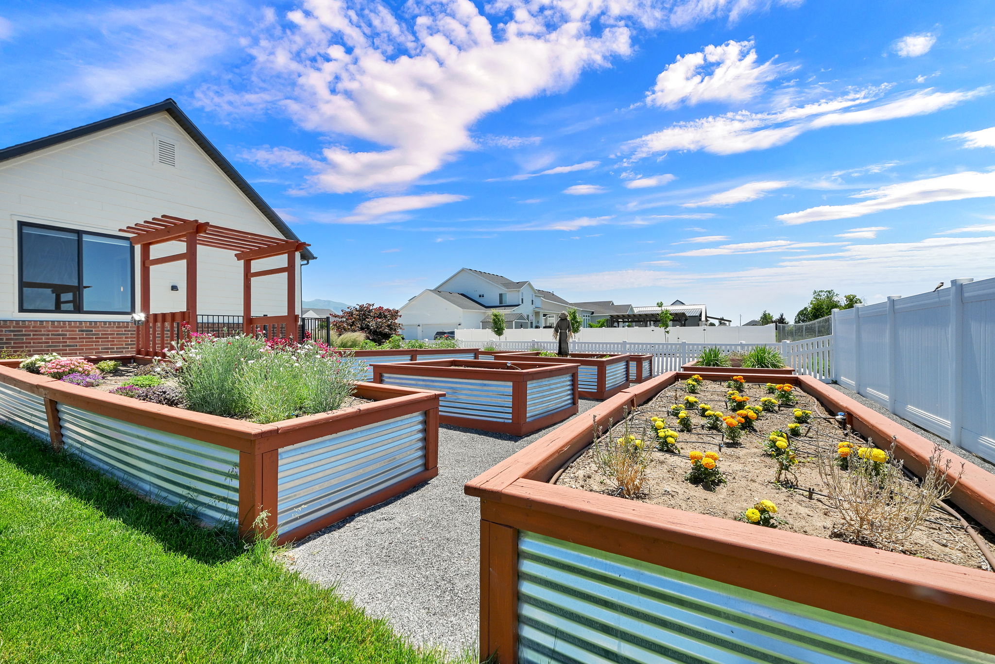 Landscaped backyard featuring multiple raised garden beds with wood and corrugated metal construction, a gravel pathway, and a privacy fence