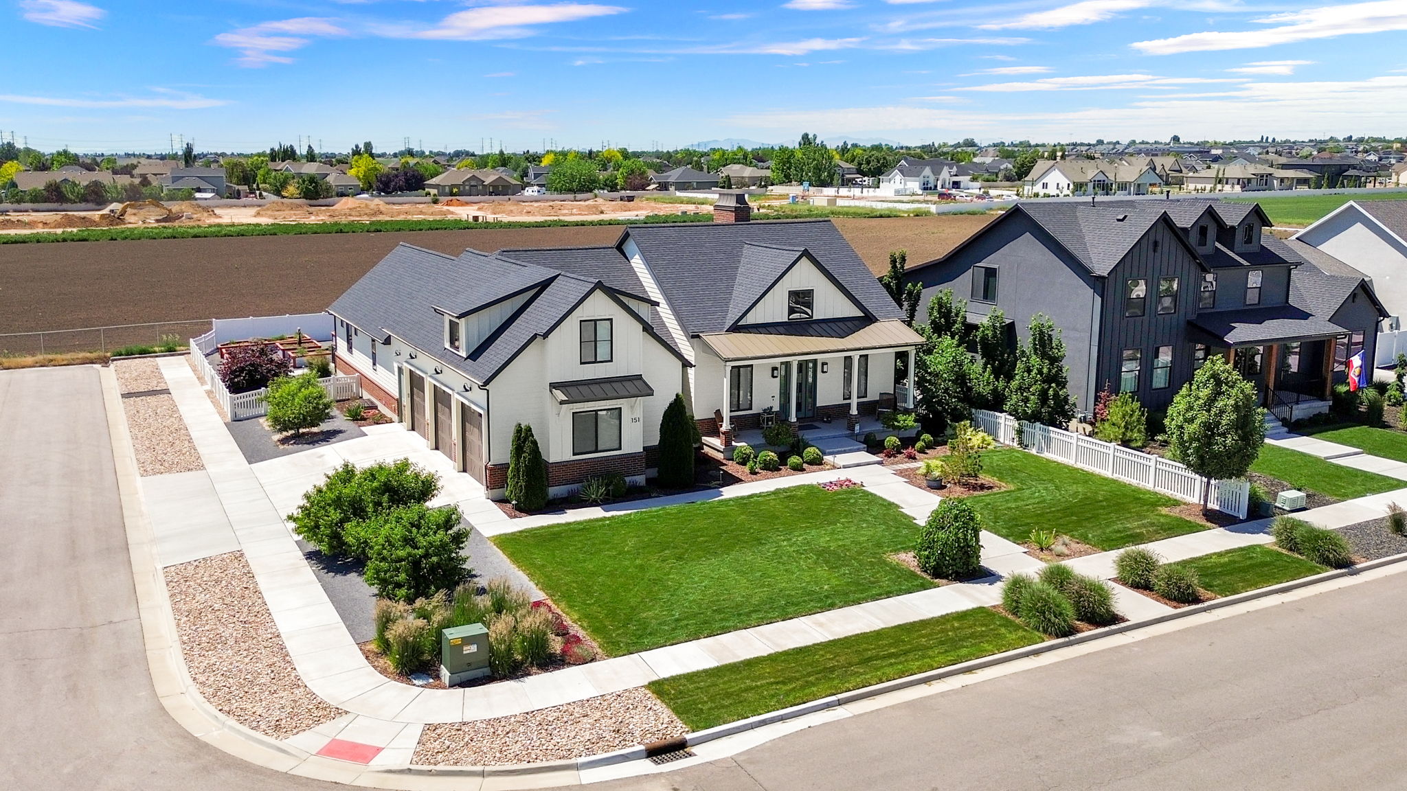 Modern Farmhouse-style residence featuring a prominent gabled roofline, an attached three-car garage with wood-finish doors, and a covered front porch with dark columns