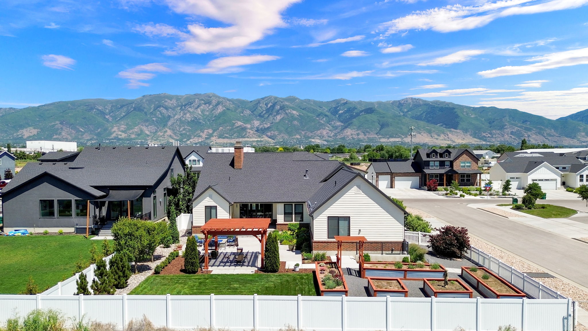 Expansive backyard featuring a large green lawn, a white privacy fence, and a wooden pergola over a patio area