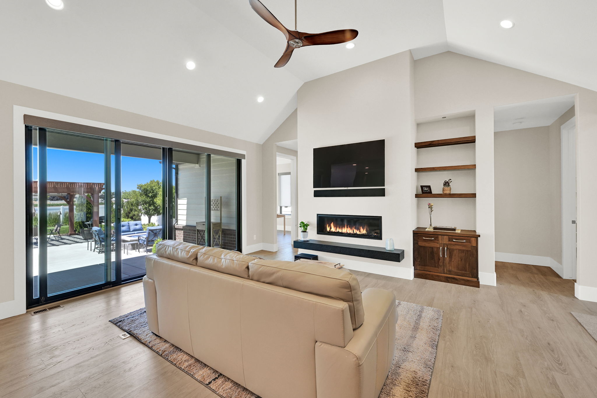 Vaulted ceilings with recessed lighting, linear fireplace, wood-finish flooring, and built-in shelving with lower cabinetry
