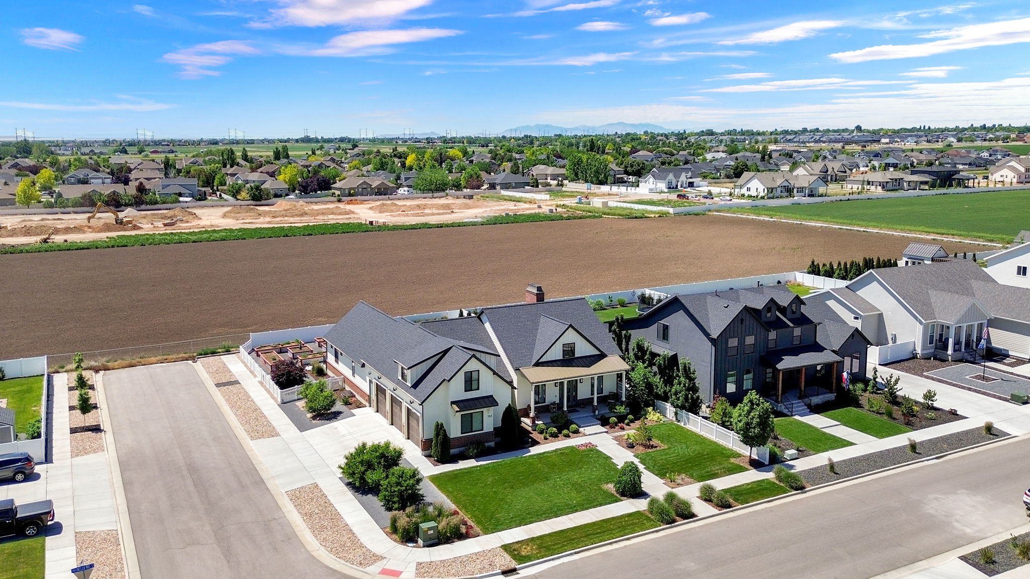 Modern farmhouse architecture featuring a light-colored exterior with dark trim accents, a covered front porch, an attached multi-car garage, and a manicured front lawn