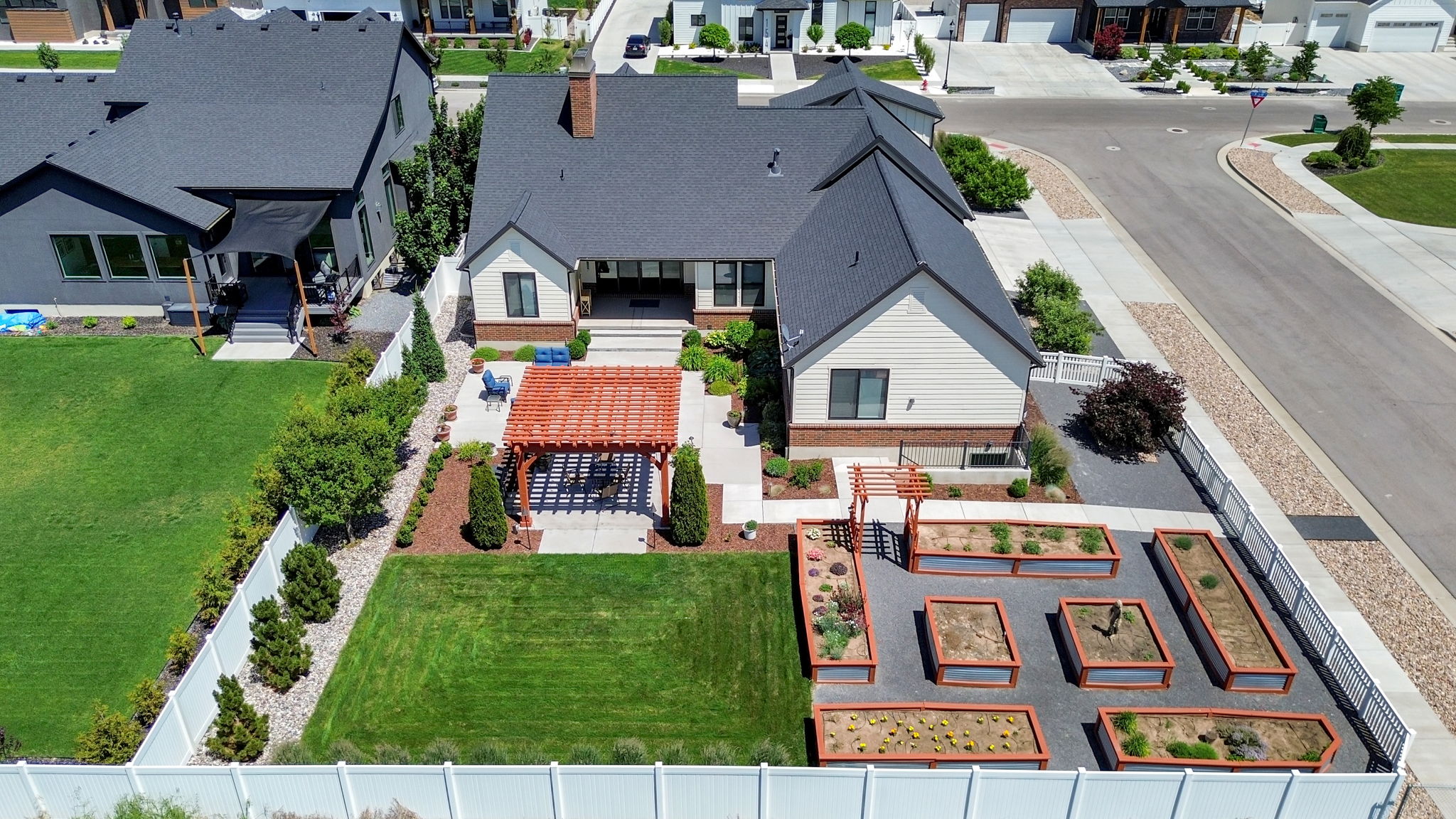 Expansive backyard featuring a lush lawn, a paved patio with a wooden pergola, and extensive raised garden beds