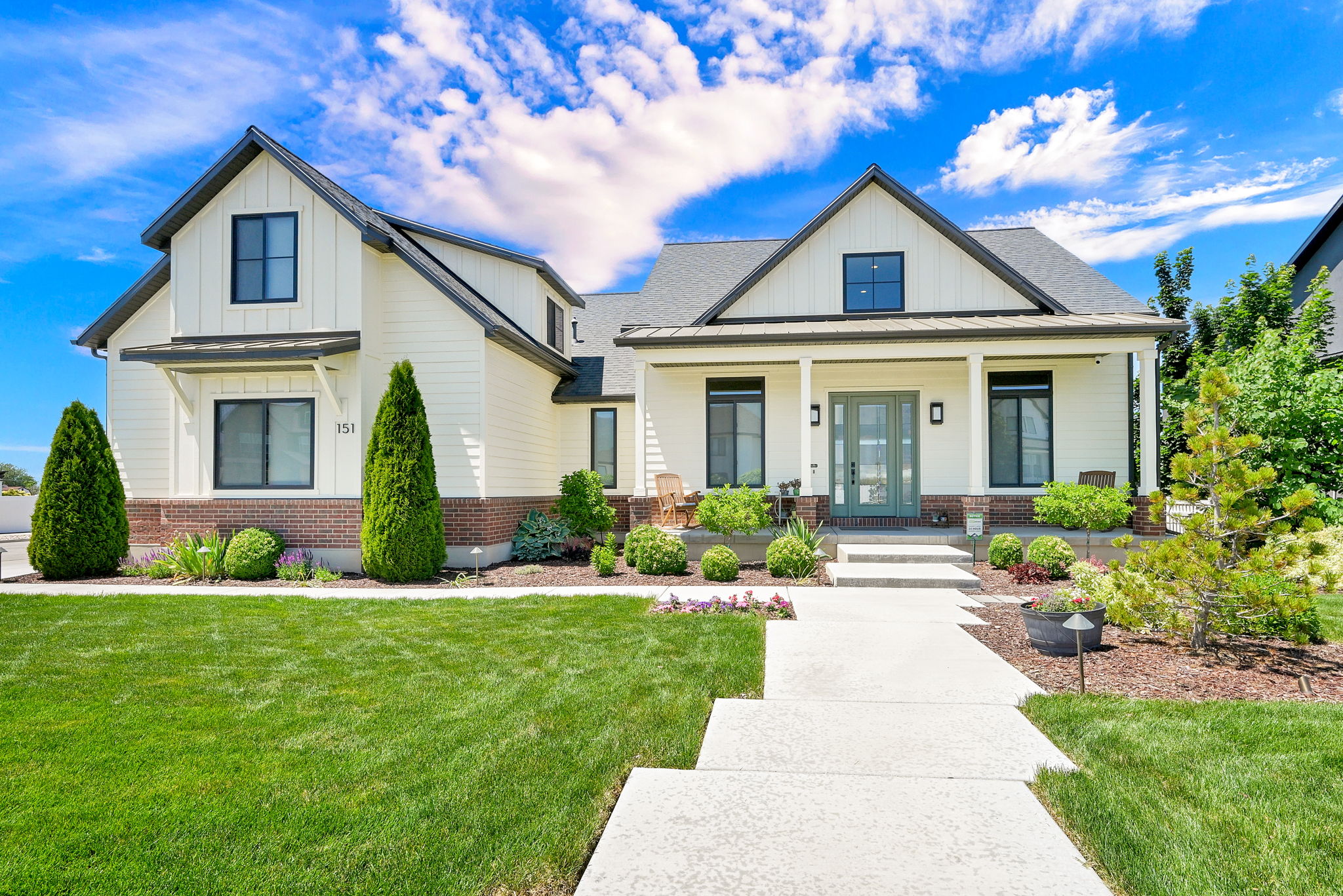 Modern farmhouse-style exterior featuring a covered porch with white columns, light siding, and dark trim windows