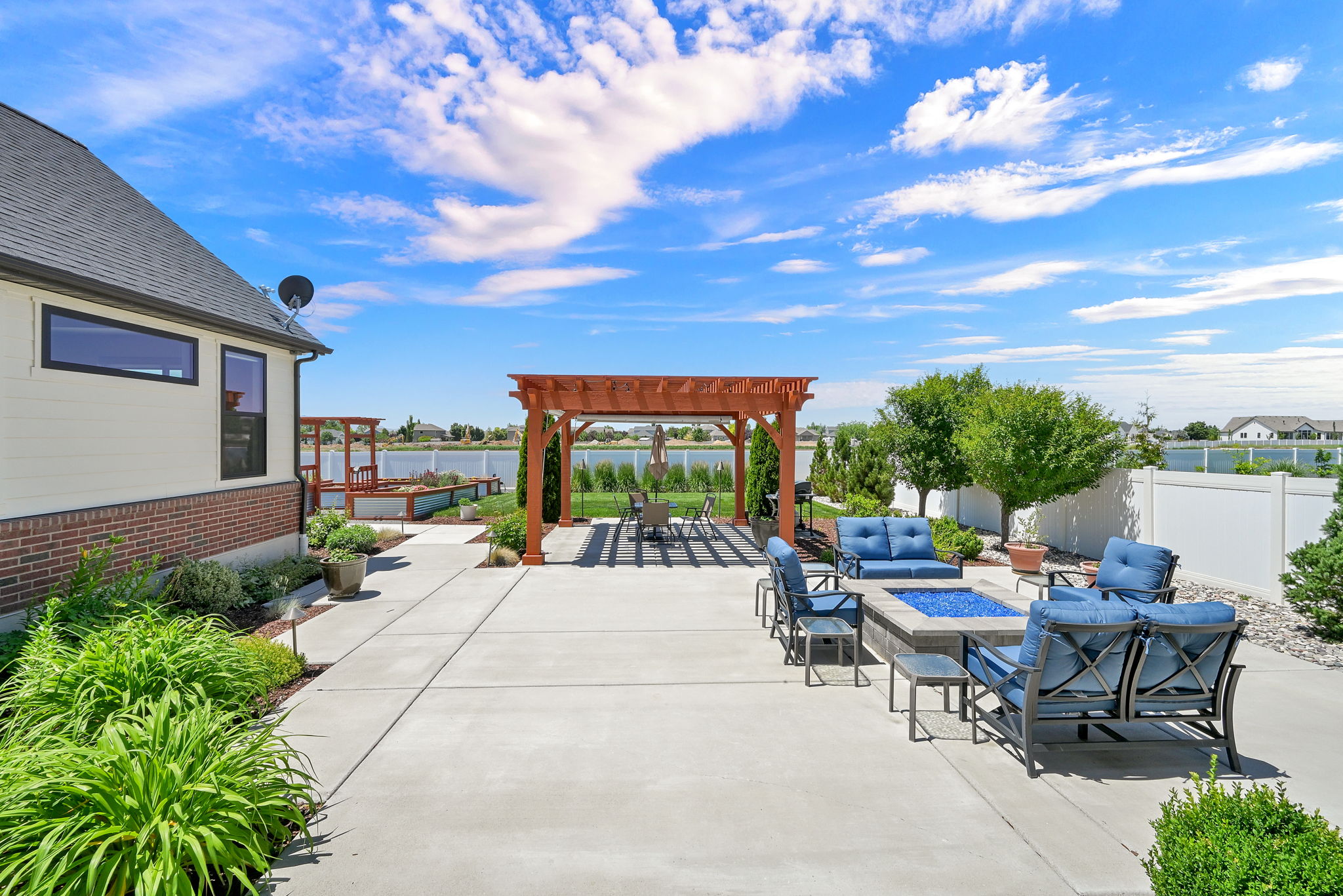 Expansive concrete patio featuring a built-in fire pit, a wooden pergola, and mature landscaping