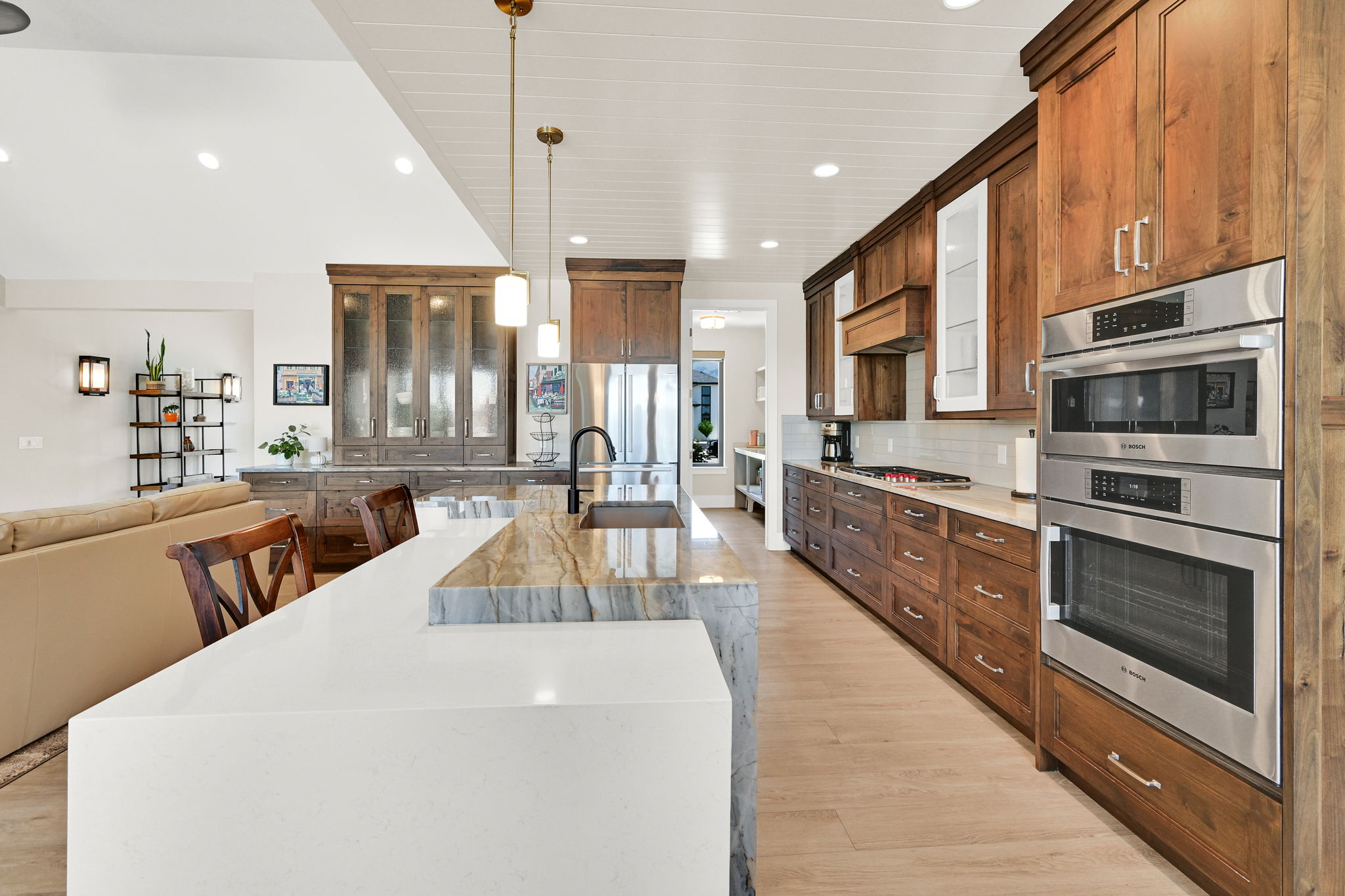 Gourmet kitchen featuring a waterfall island with a white solid surface countertop, a second island with a stone countertop and undermount sink, rich wood cabinetry, stainless steel double wall ovens, and wood-finish flooring