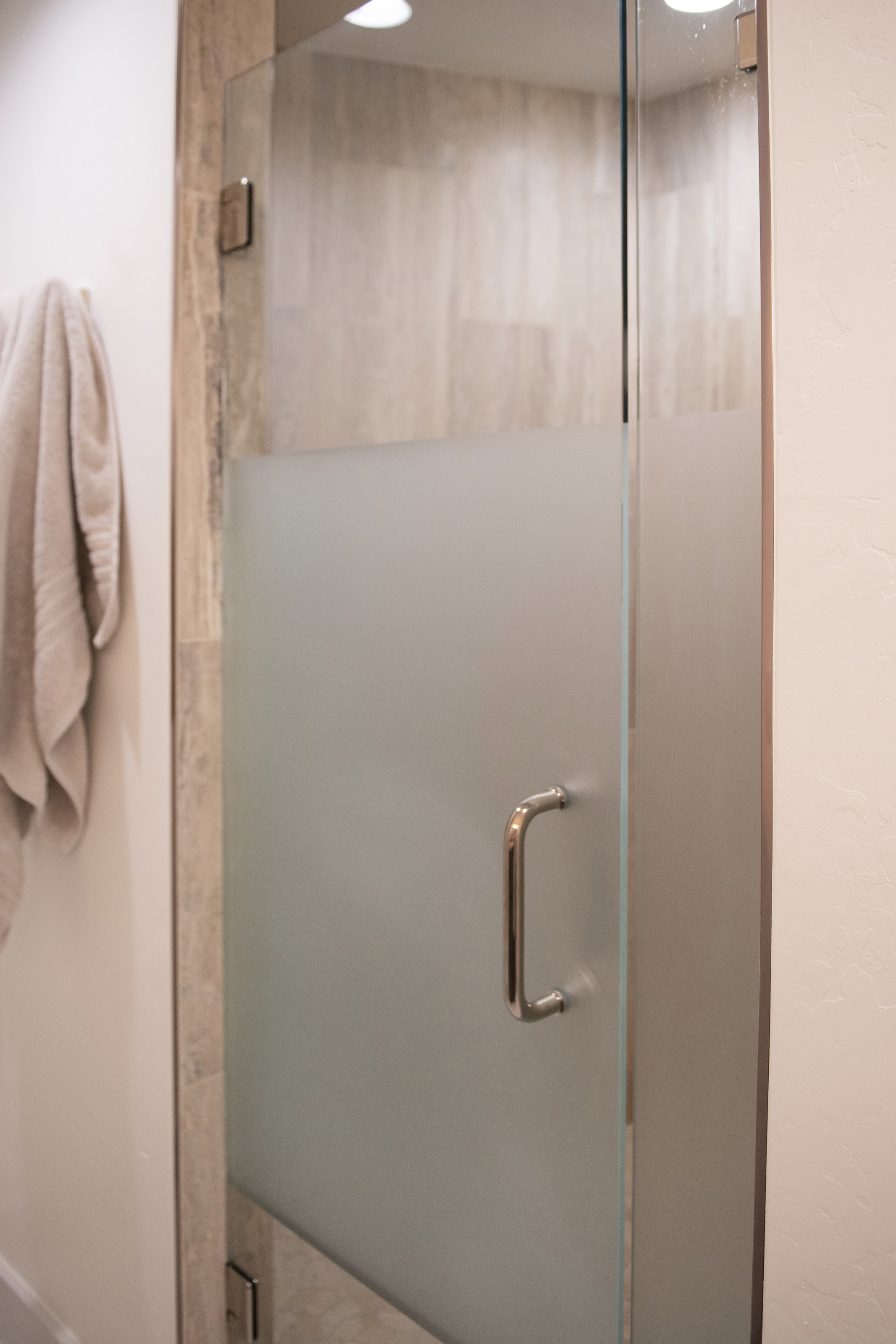 Frosted glass shower enclosure featuring polished chrome hardware, full-height tile surround, and recessed overhead lighting