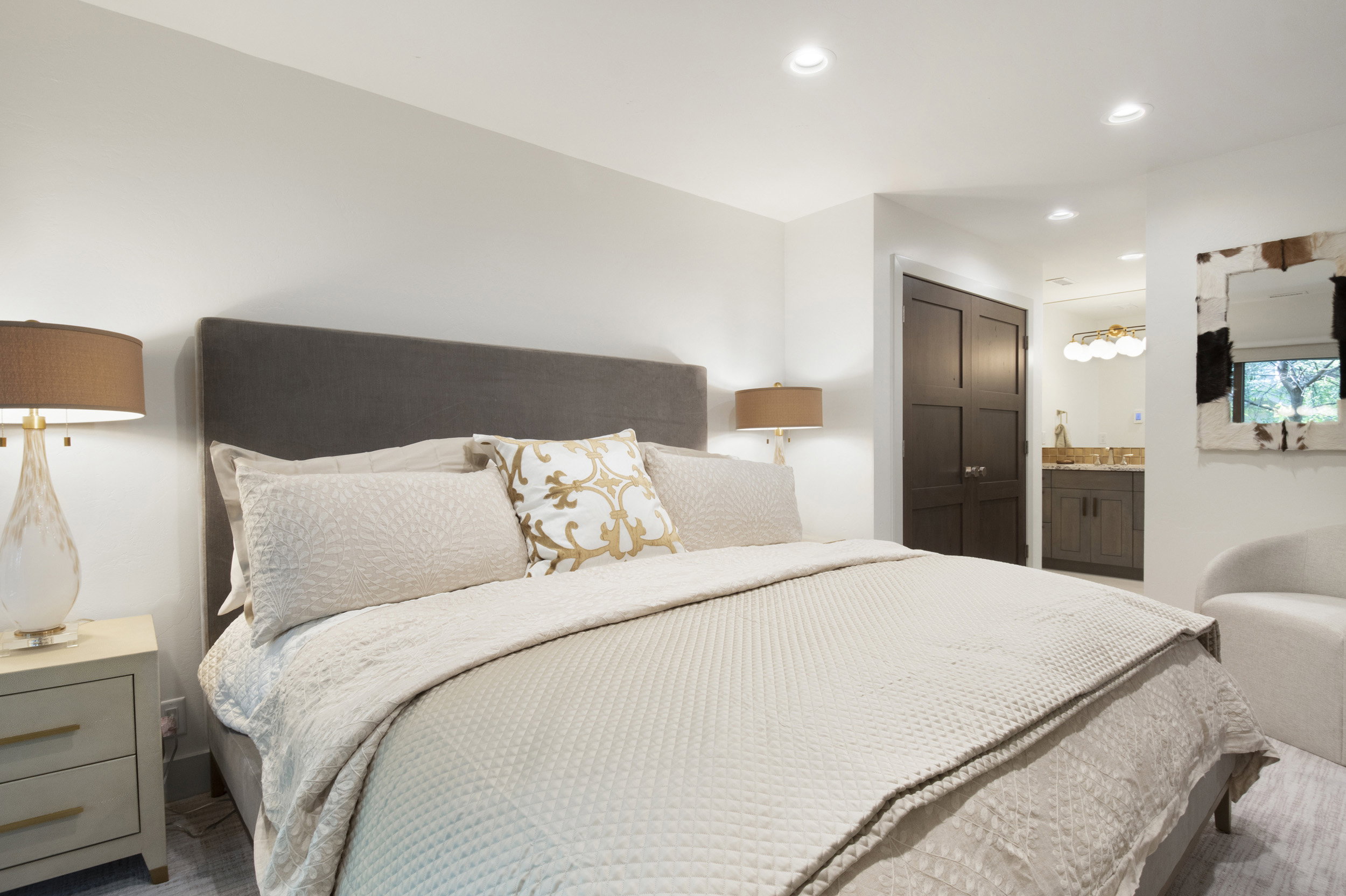 Recessed lighting illuminates this bedroom featuring a dark wood-finish paneled door, a bathroom vanity with a basin sink, and a multi-bulb vanity light fixture